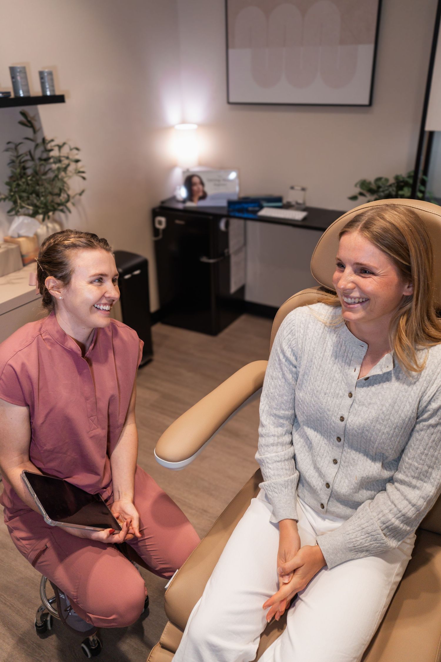 Two people sit together in an office setting, engaged in conversation and sharing laughter.