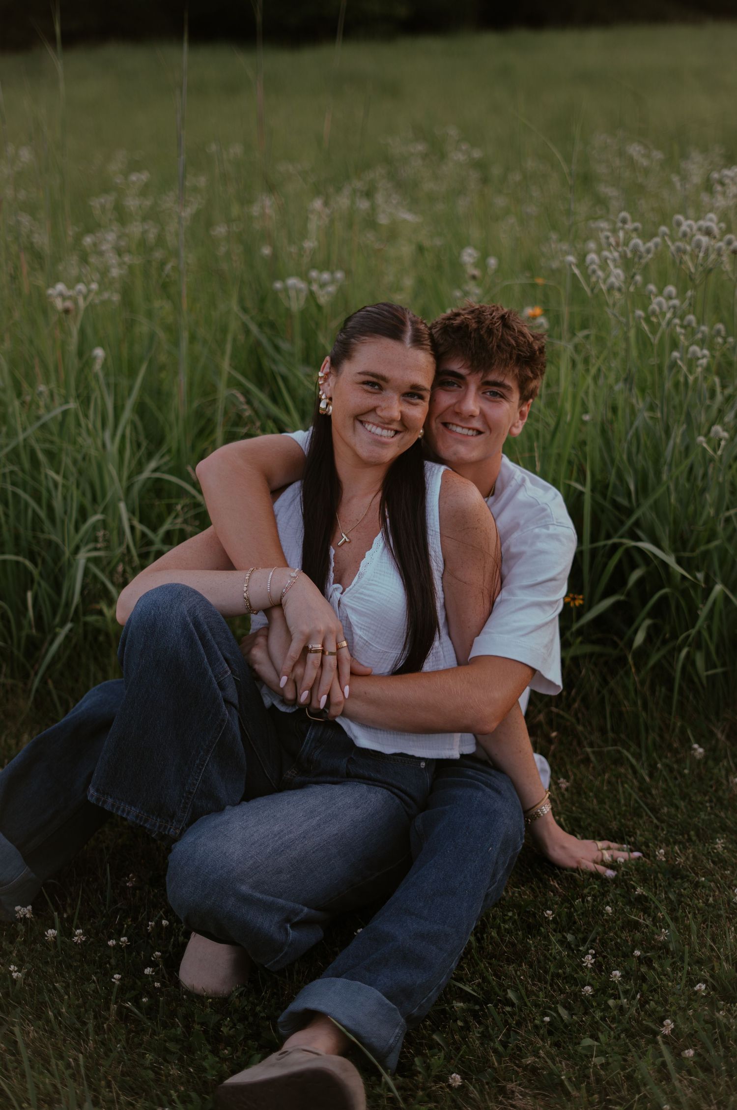 Couple sitting in a wildflower meadow, smiling and embracing during golden hour.