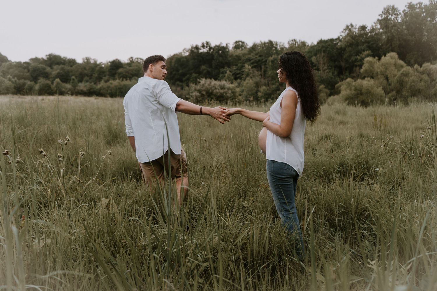 Two people holding hands while standing in a tall grass field during sunset.