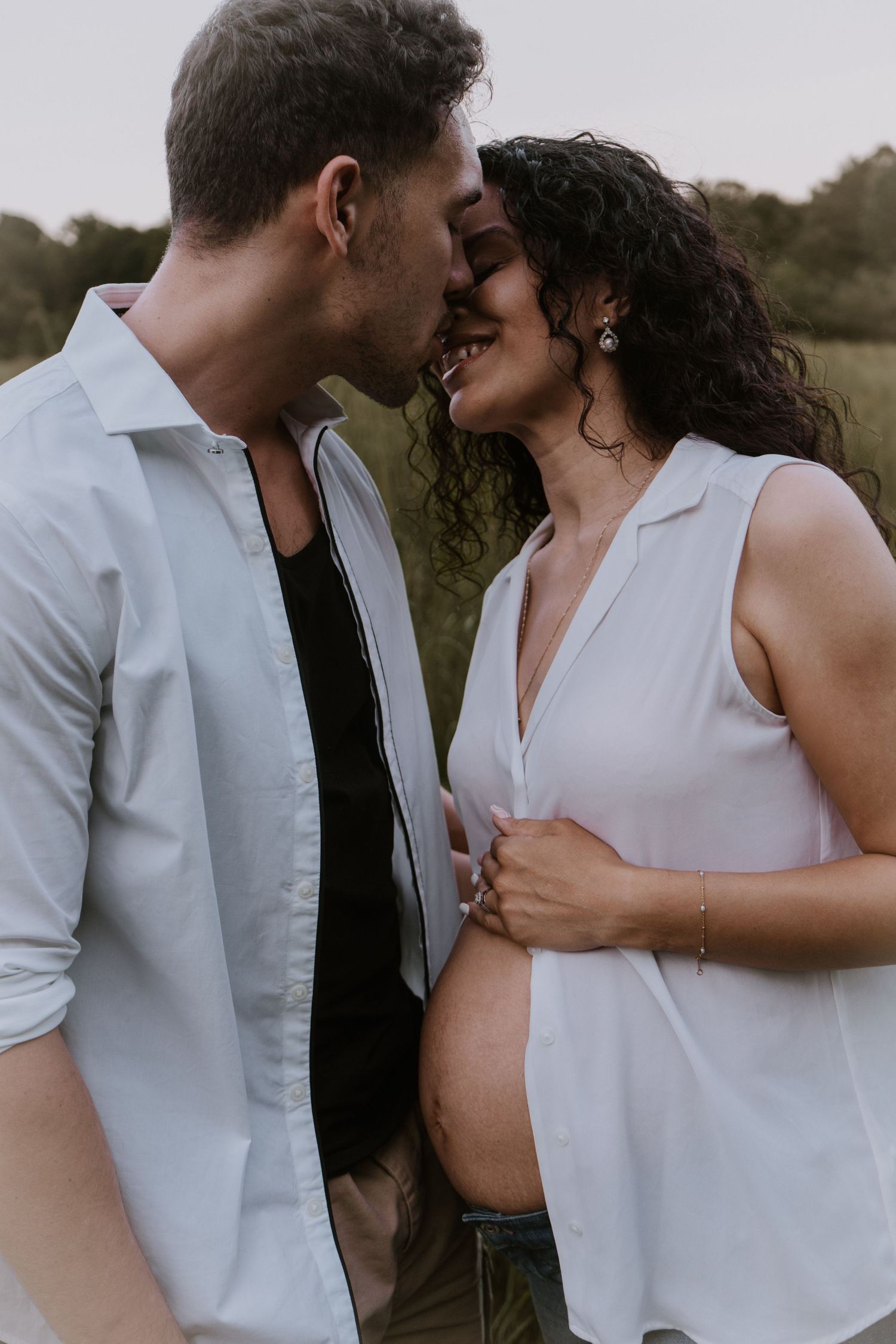 A romantic couple shares tender moments in matching white outfits during an outdoor photoshoot.