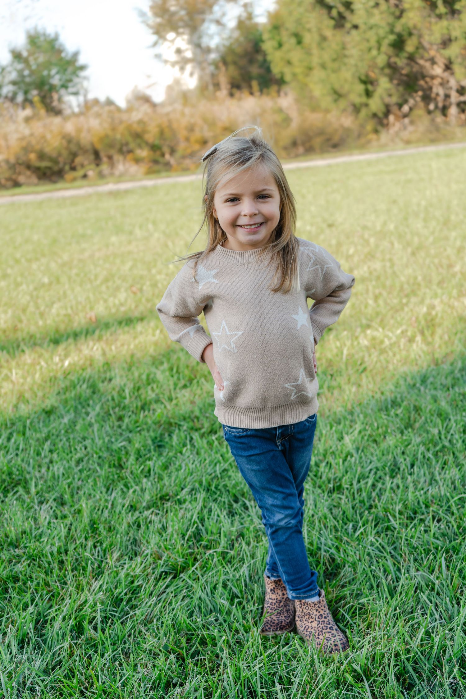 A child wearing a beige sweater and jeans runs joyfully through a grassy field on a sunny autumn day.