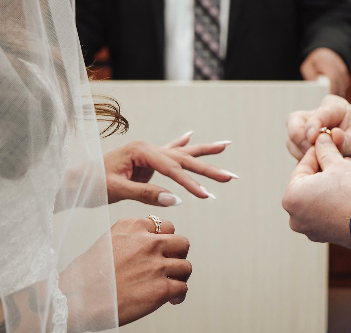 Close-up of a bride and groom exchanging wedding rings during a ceremony, with the bride wearing a veil.