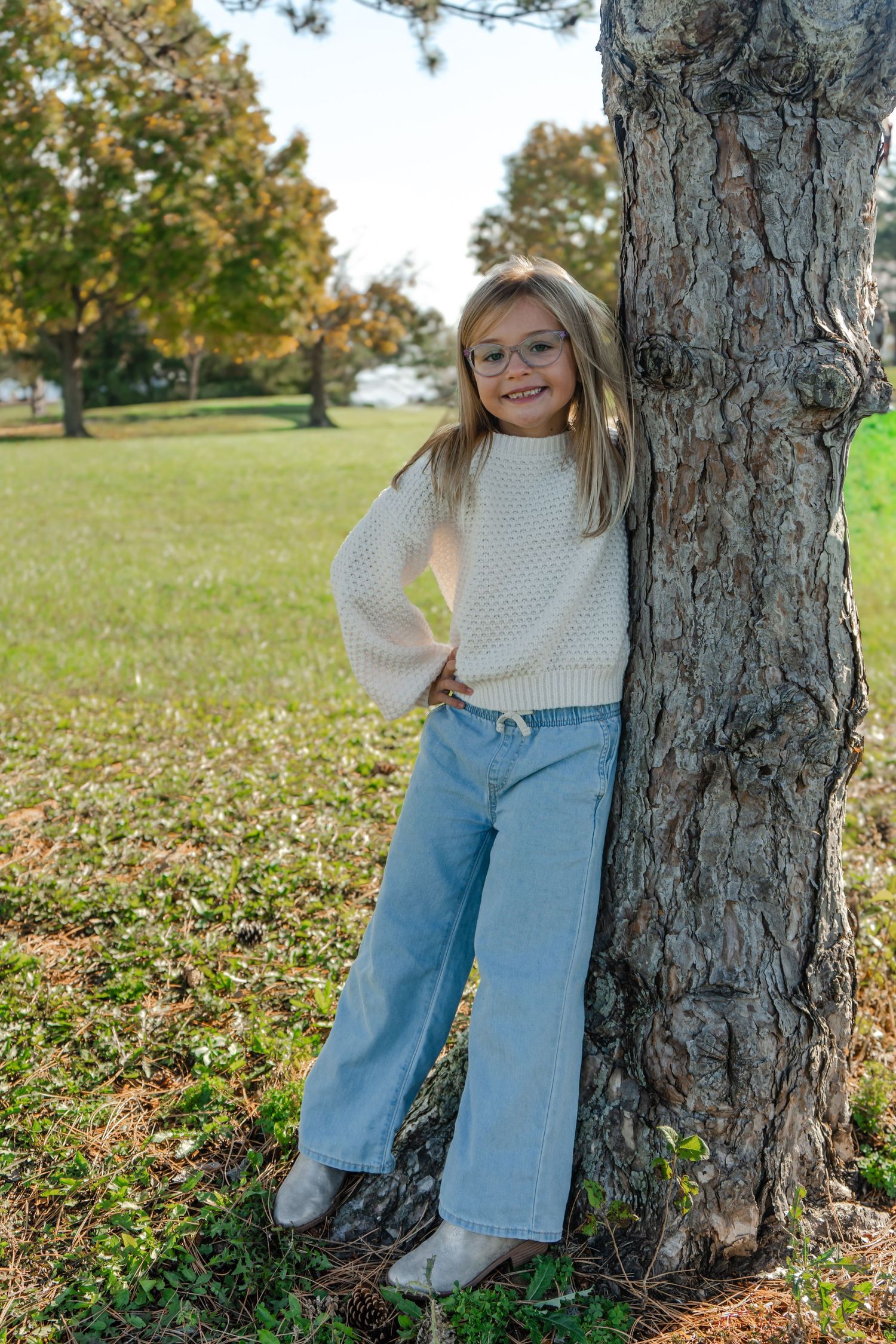 A series of candid poses next to a large tree trunk in a park with fallen autumn leaves.