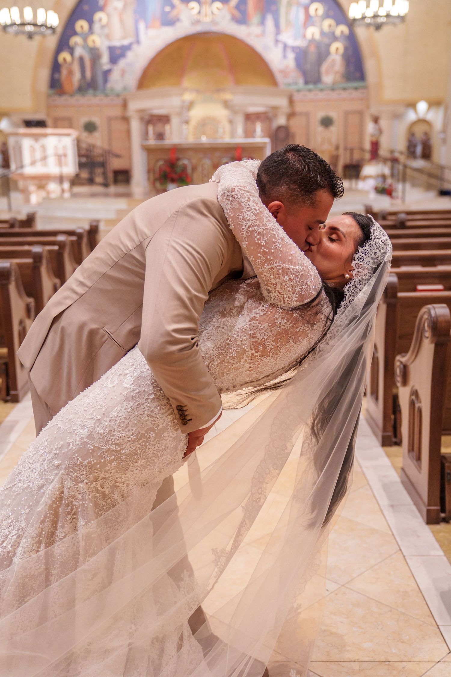 A groom dips and kisses his bride in a stunning church wedding ceremony, her lace gown and veil flowing gracefully.