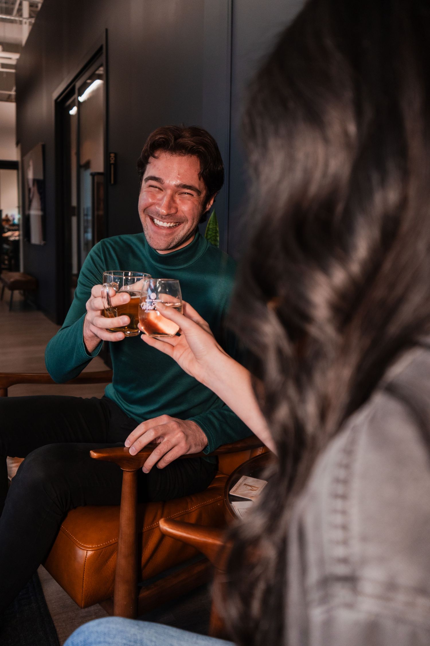 Two friends share a laugh while toasting drinks at a dimly lit bar.