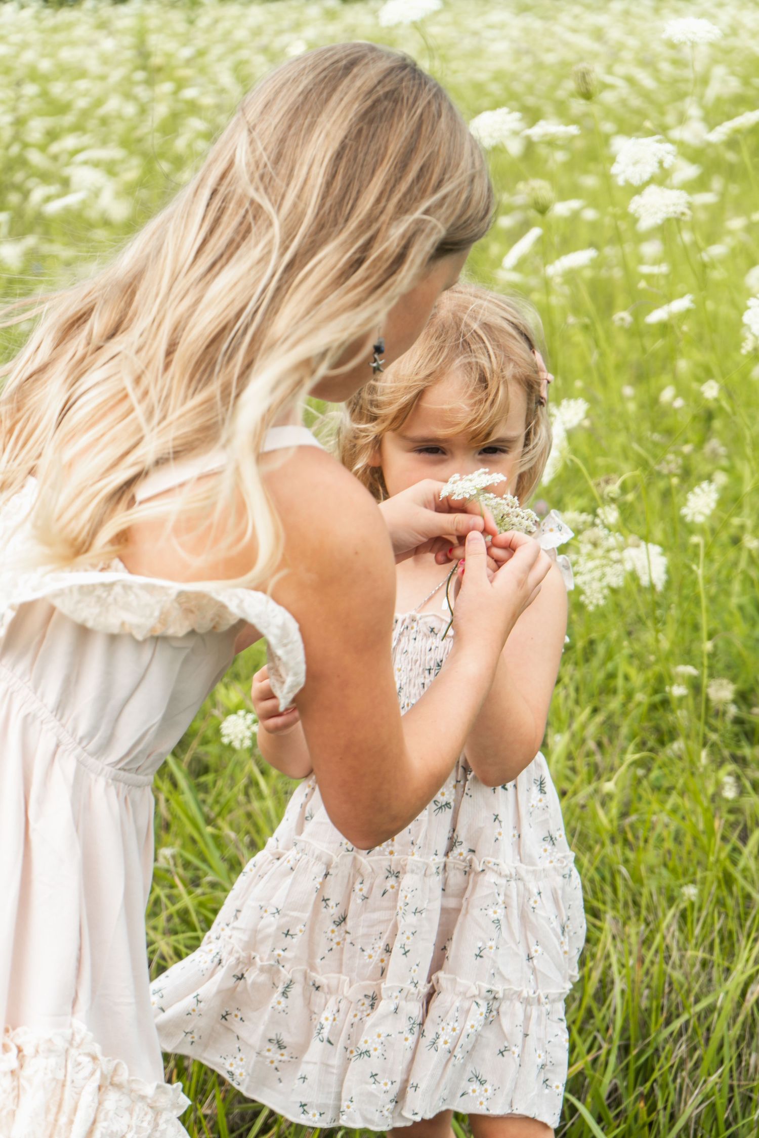 A tender moment shared between two in white dresses among tall grass and wildflowers.