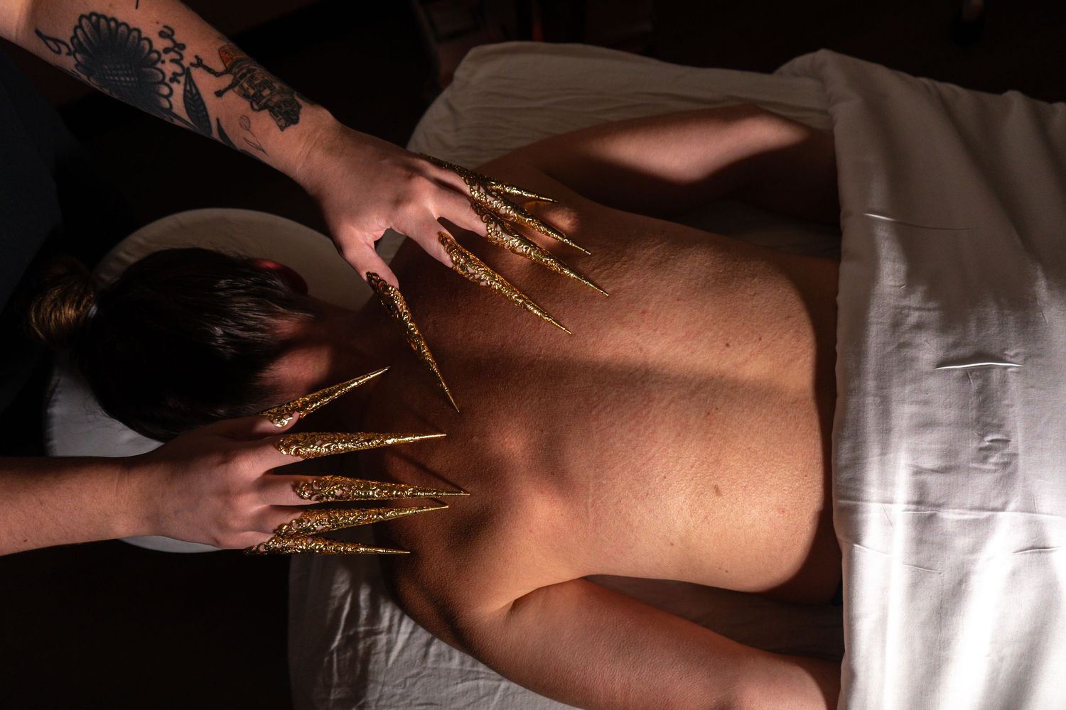 Hands performing therapeutic massage with gold glitter on a person's back during a spa treatment.