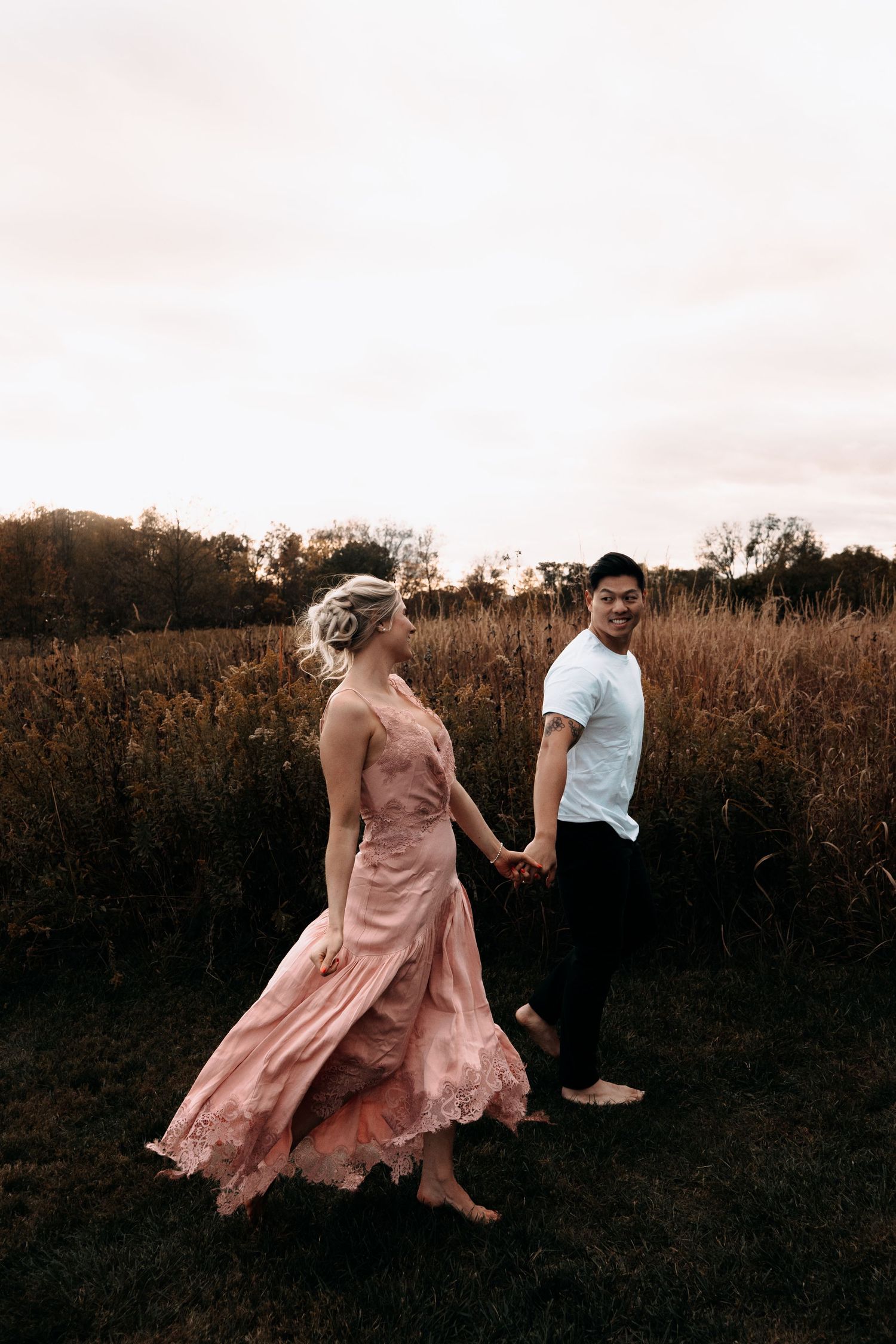 A couple dances together in a field at sunset, with the woman's pink dress flowing gracefully in motion.