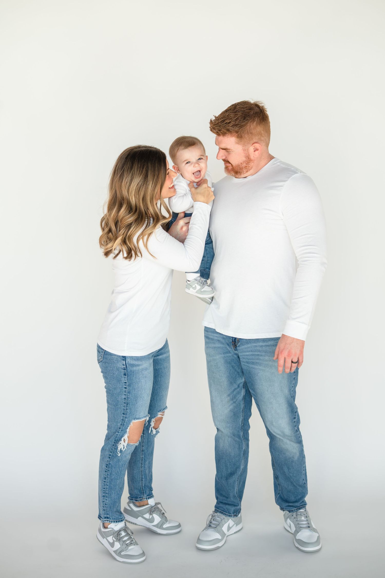 Parent and child wearing matching white shirts and blue jeans pose playfully in sequence of four photos against white wall.