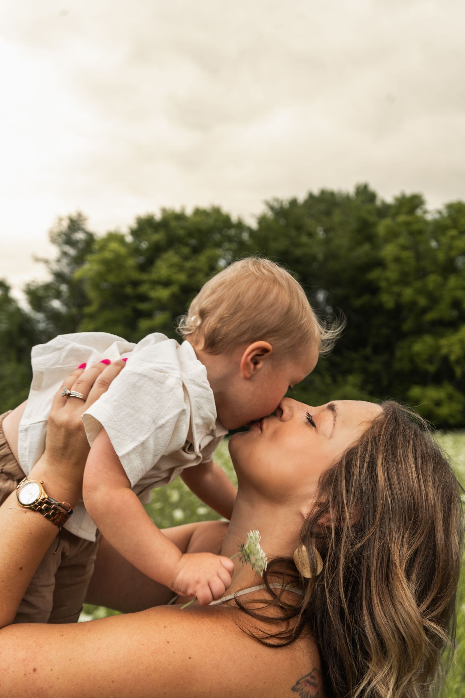 A mother playing with her baby outdoors in a green field on a cloudy day.