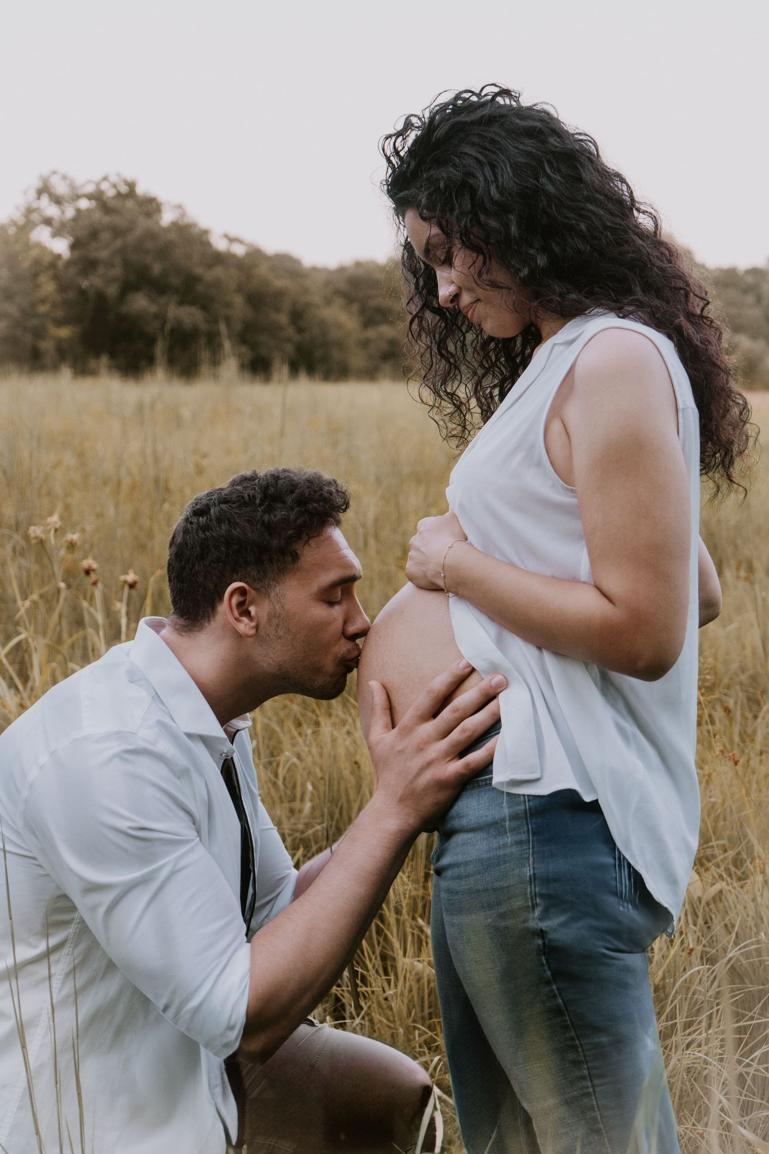 Tender maternity moment as couple embraces in golden field during pregnancy photoshoot at sunset.