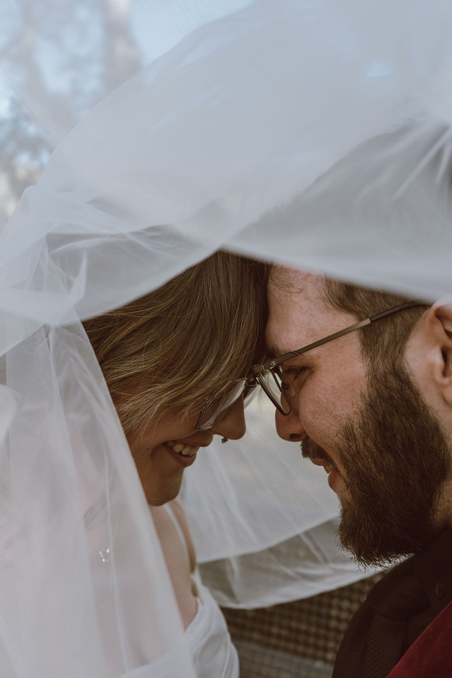 A romantic close-up moment under a flowing white veil during a wedding photoshoot.