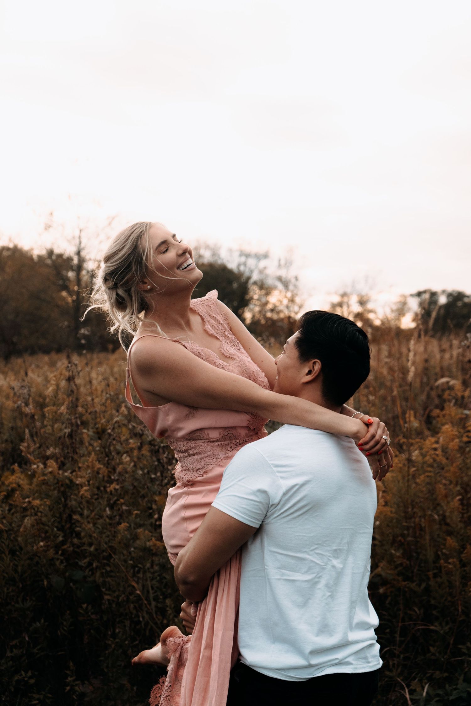 Romantic couple embracing and laughing together in a golden autumn field at sunset.