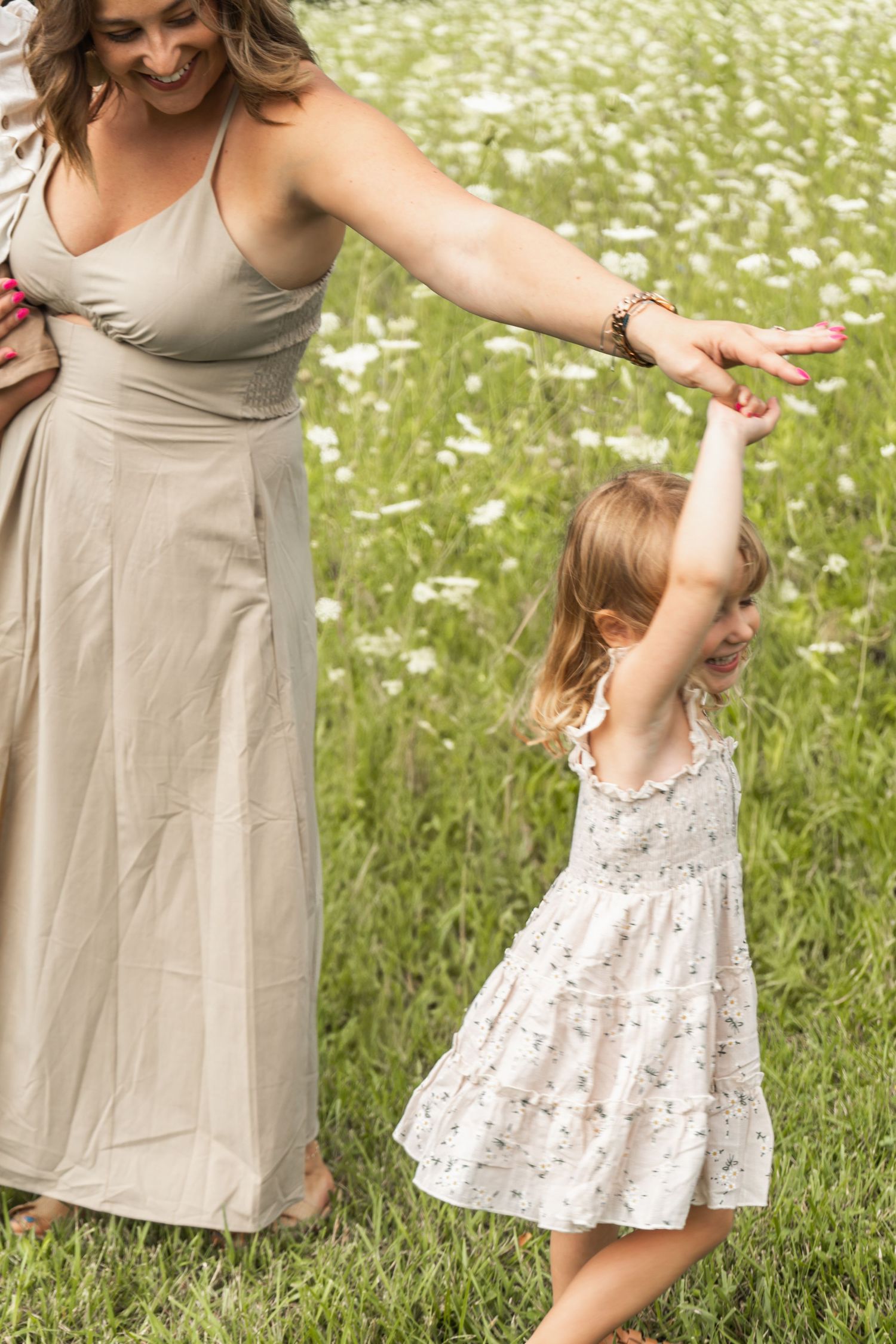 Two figures in light dresses dance and hold hands in a wildflower meadow on a sunny summer day.