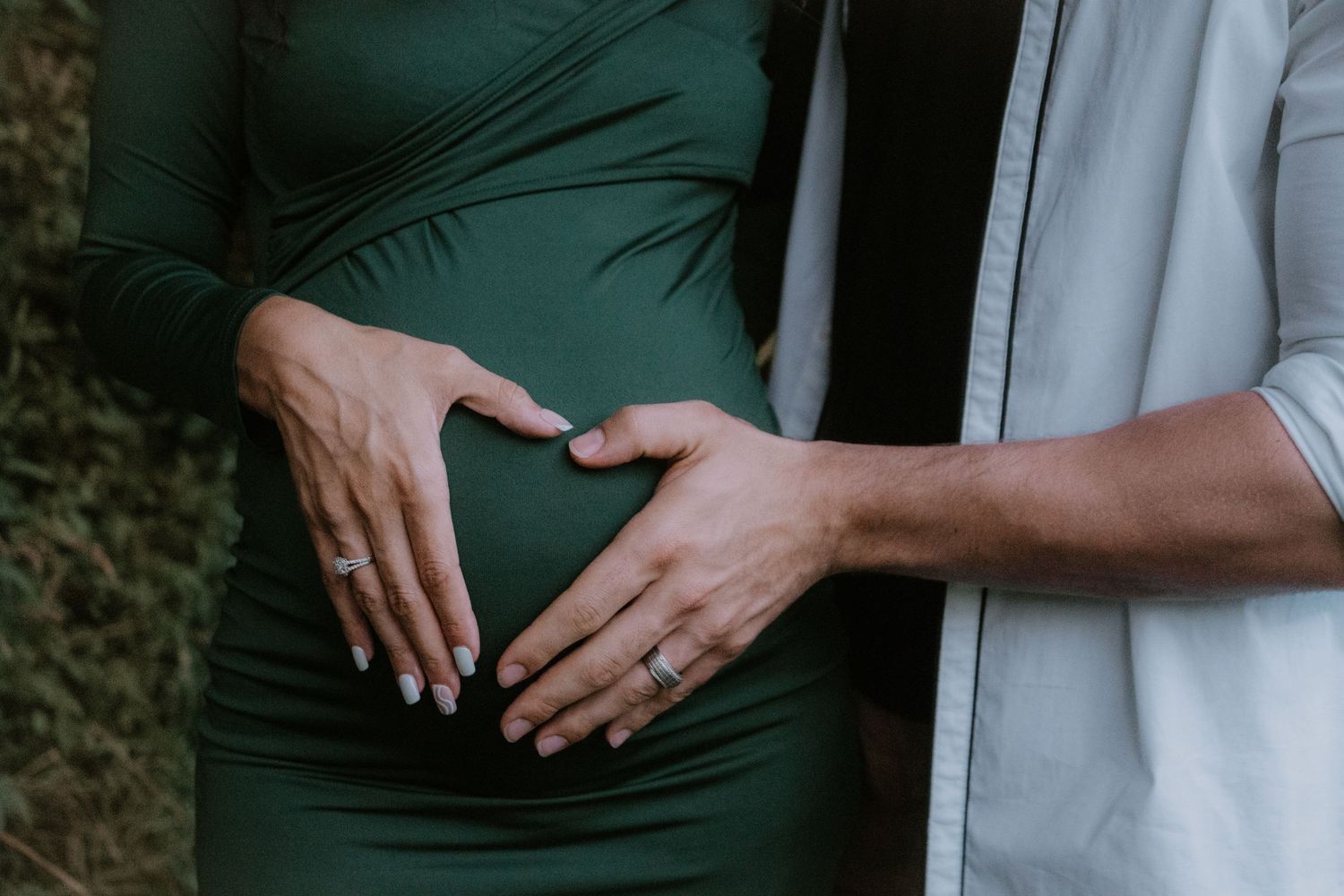Close-up shot of hands gently touching a pregnant woman's belly while wearing white and green clothing.