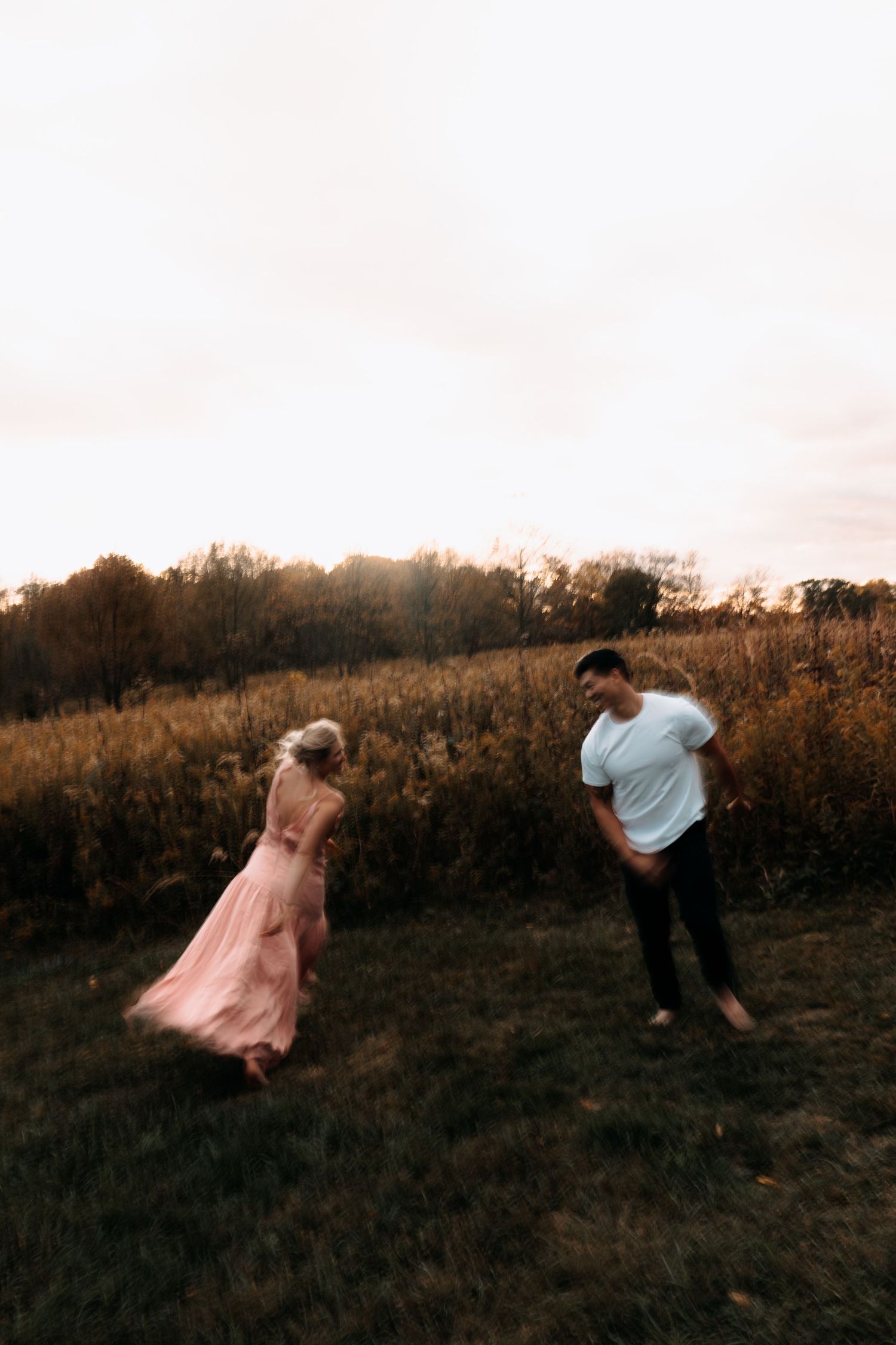 Couple dancing in a golden field at sunset, woman in flowing pink gown, man in white shirt and dark pants.