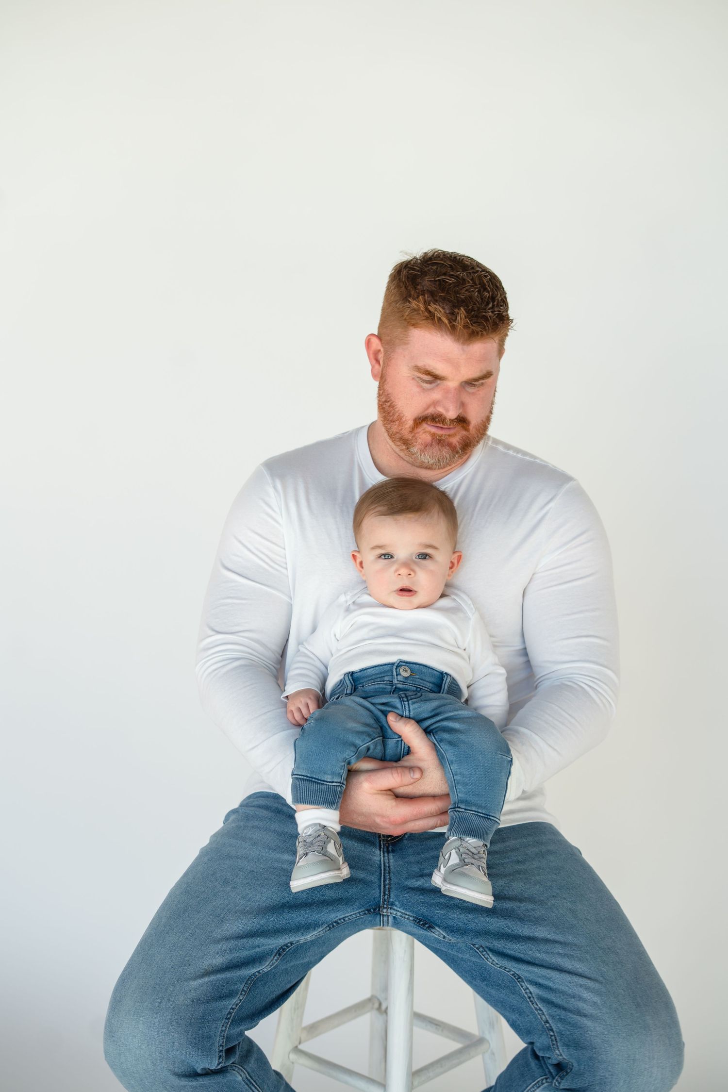 Parent and child sit together on white stool against light background in matching outfits.