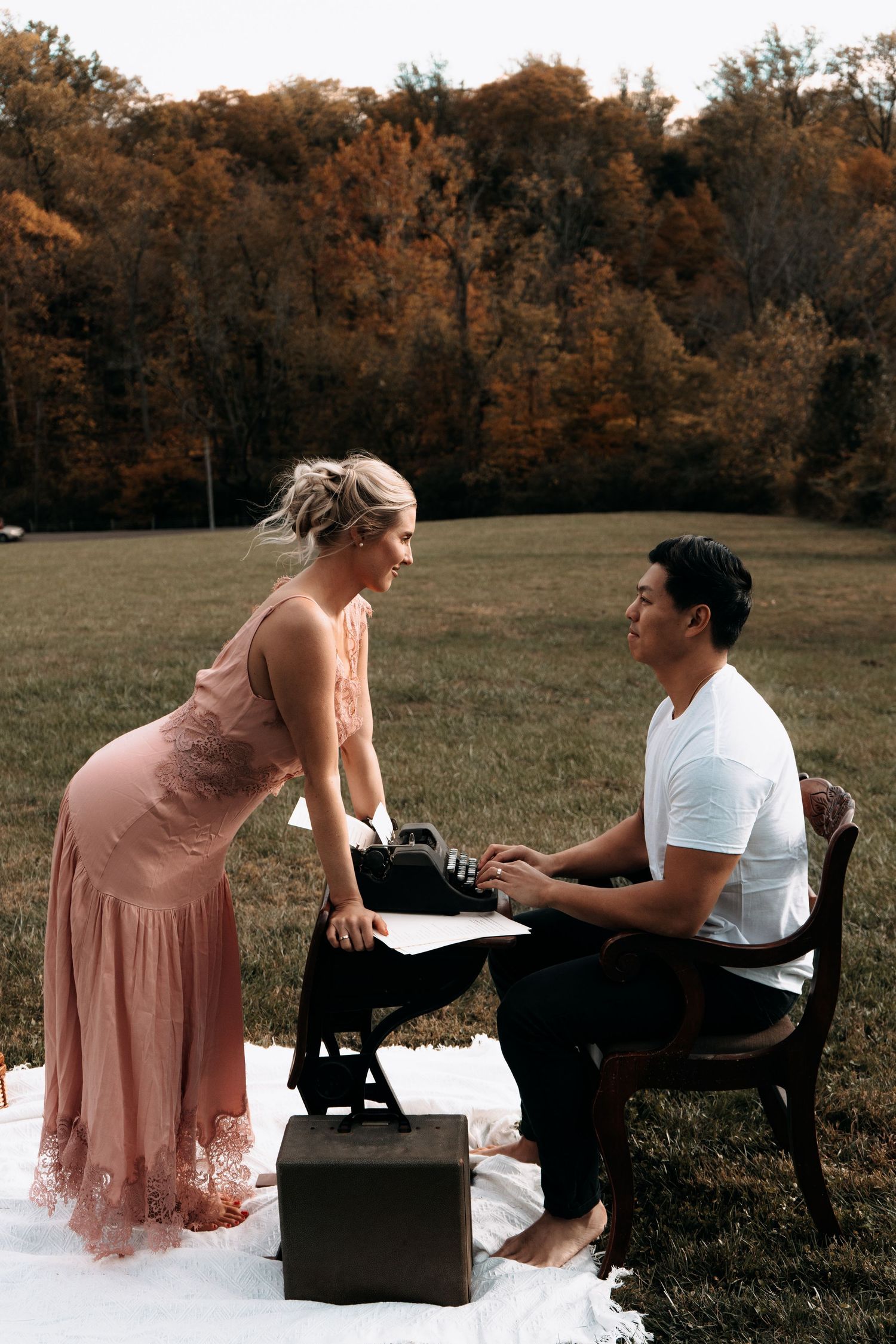 A couple sits together on a park bench surrounded by autumn trees in a romantic outdoor photoshoot.