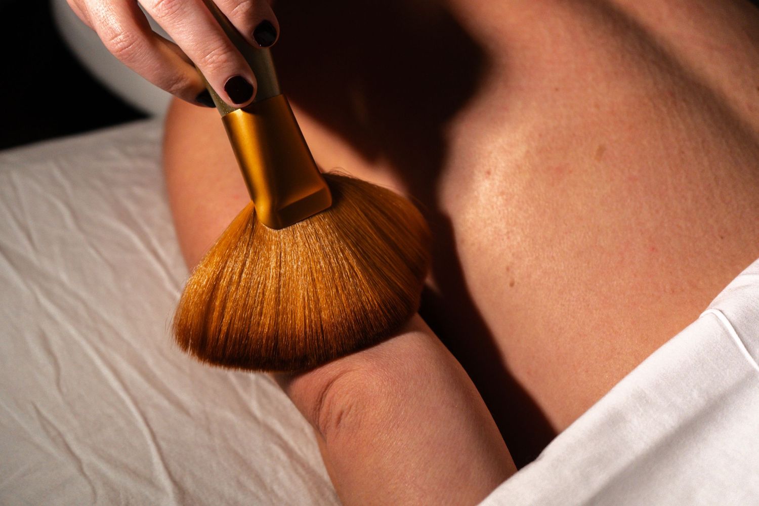 Close up of makeup brush applying powder blush or bronzer to cheek in a sweeping motion.