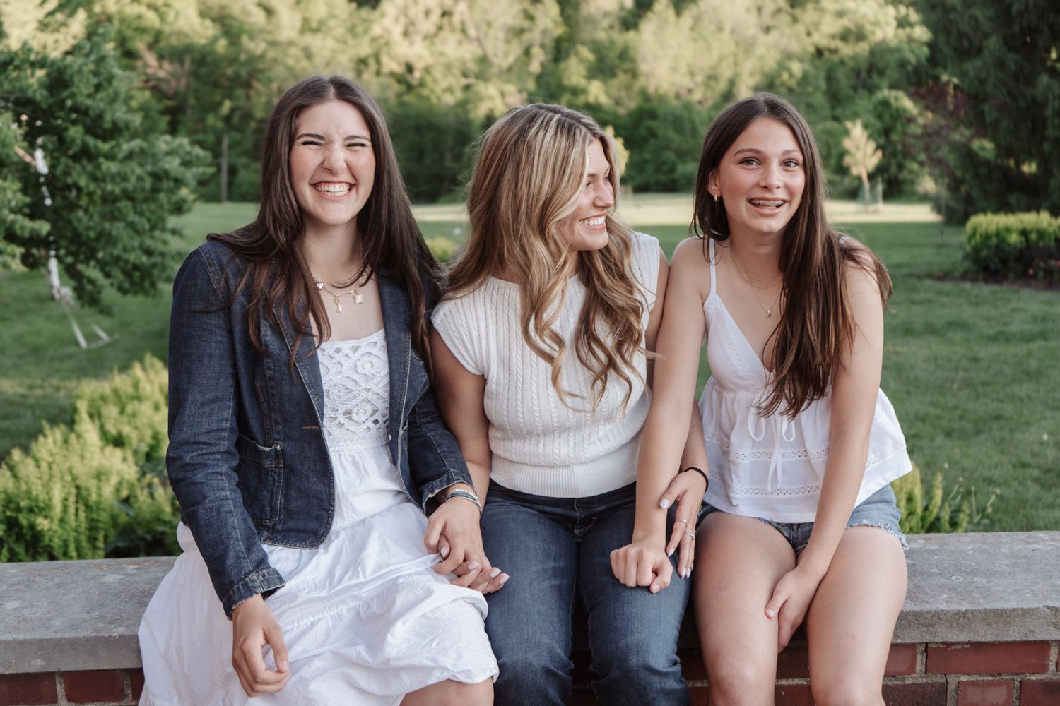 Three friends sitting together on a bench in a lush garden setting.