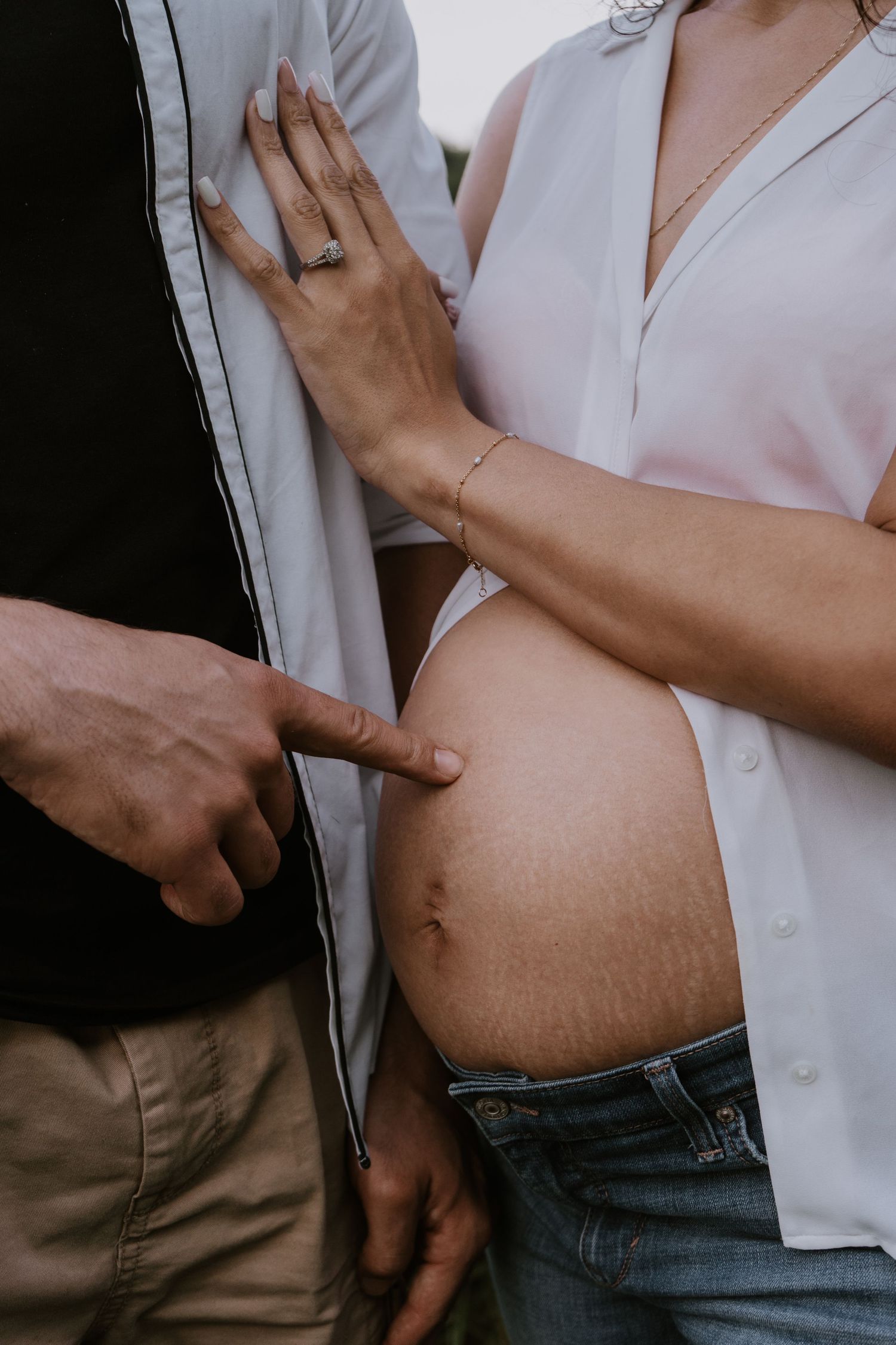 Couple sharing intimate moment with hands on pregnant belly wearing white shirt and jeans.