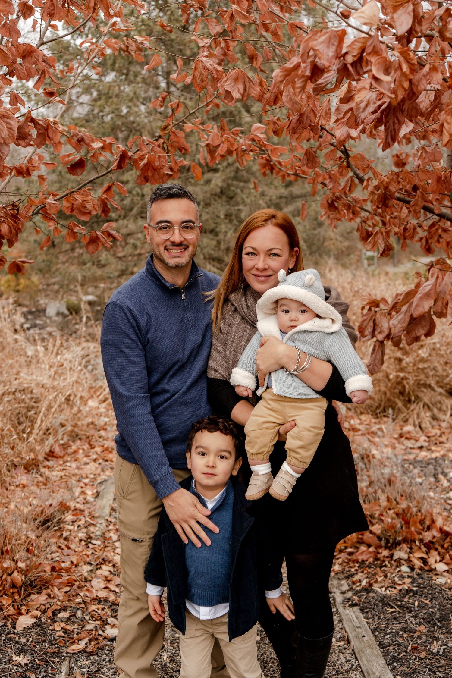 A family poses together outdoors in autumn with red leaves in the background.