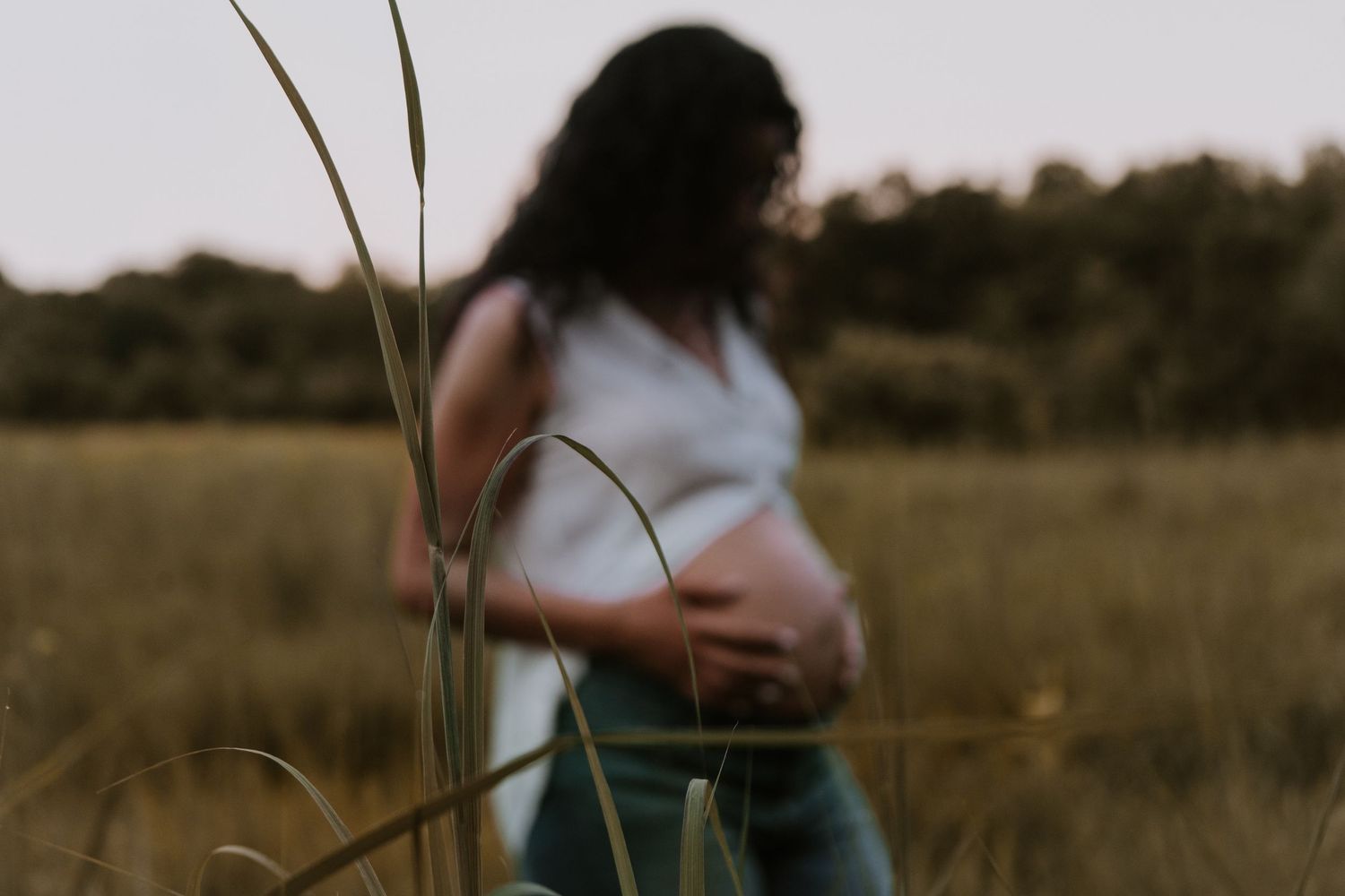 A couple stands close together in a peaceful grassy field during golden hour.