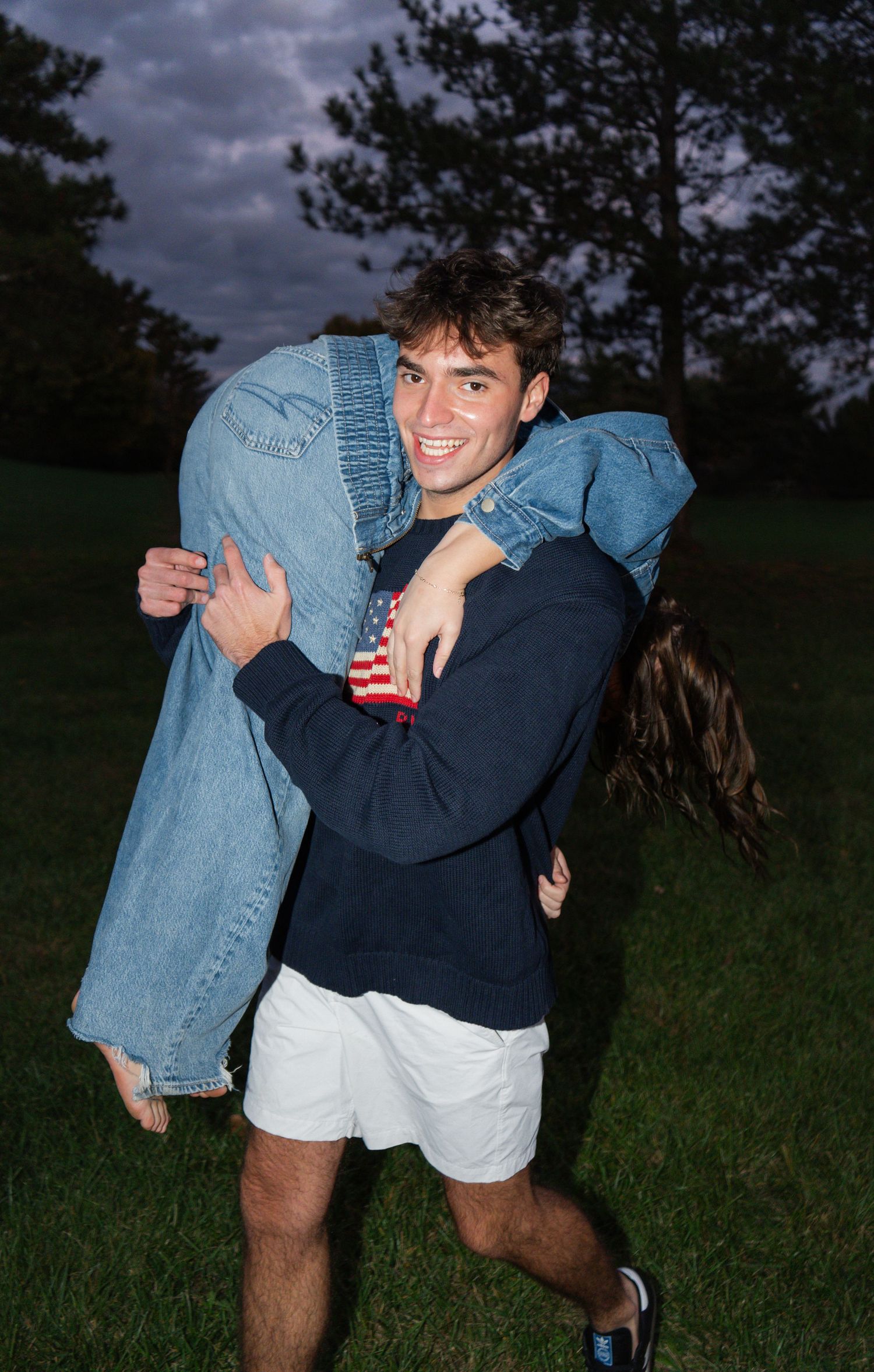 Two people playfully interact outdoors wearing casual denim and navy clothing against a moody sky.