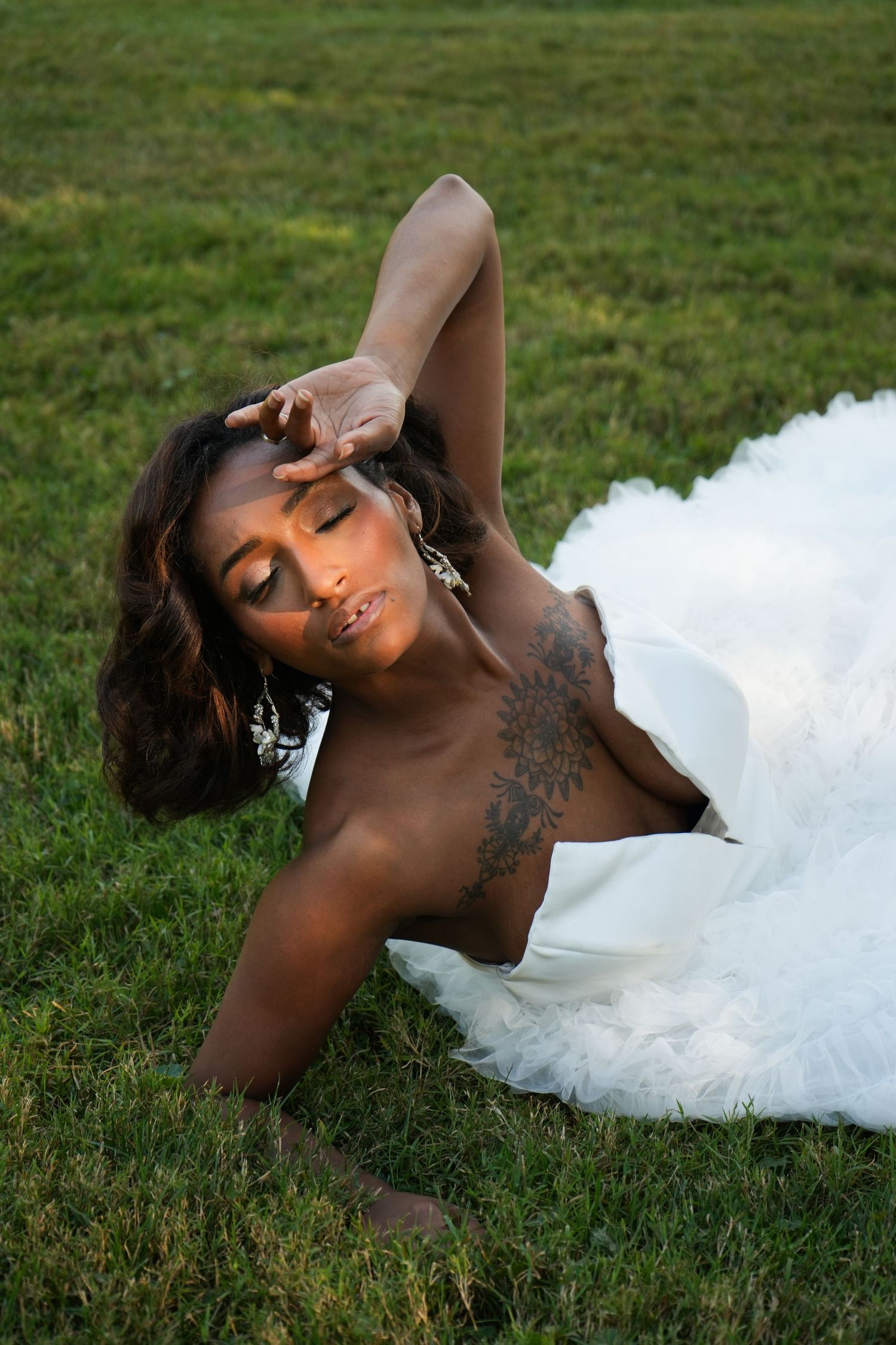 A woman in a white wedding dress poses gracefully on green grass during an outdoor bridal photo session.