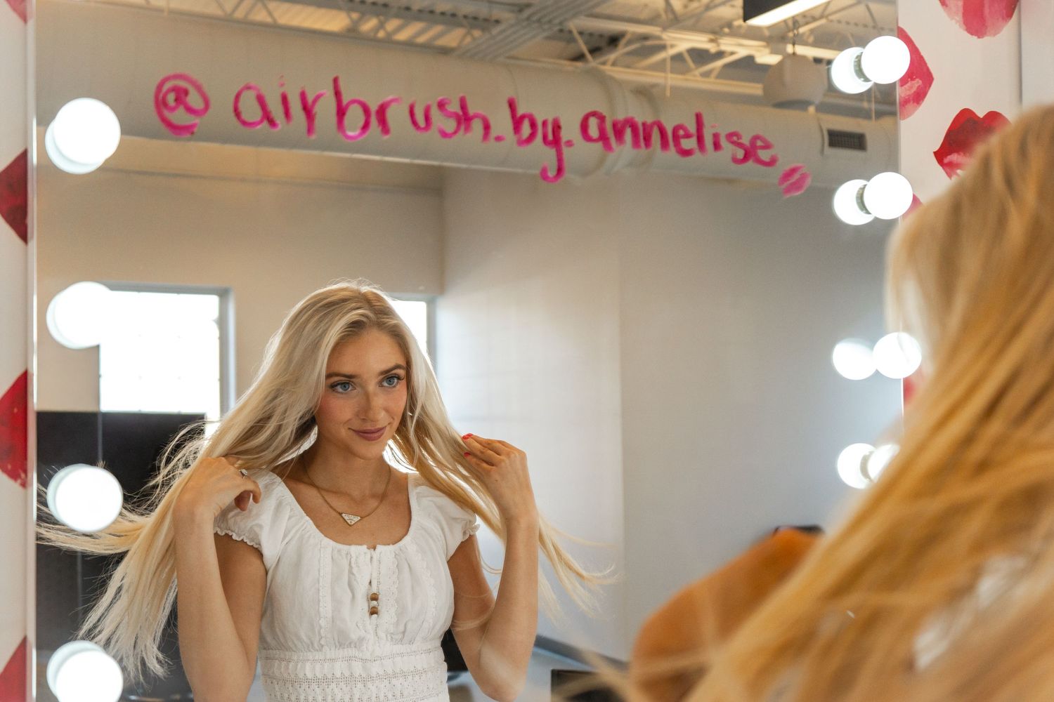 A bright retail space with white vanity mirrors and pink accents displays airbrush makeup services and products.