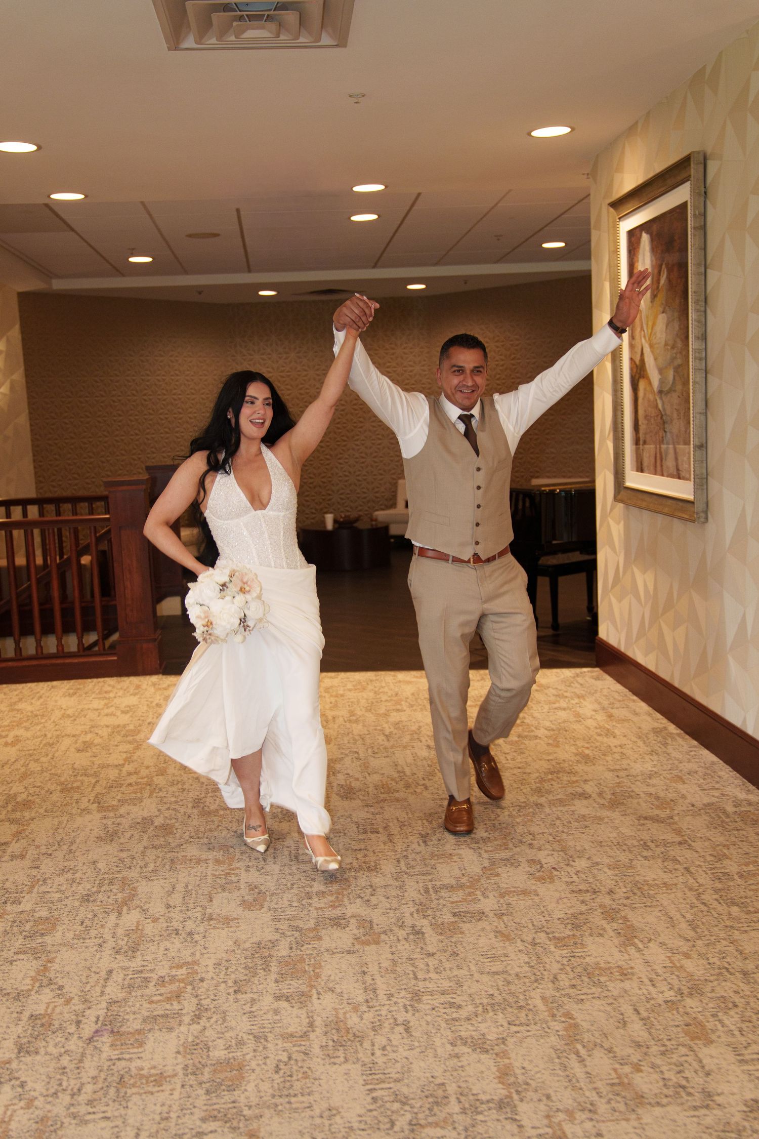 Joyful newlyweds celebrate their wedding day, bride in white gown holding bouquet, groom in tan suit, raising hands triumphantly.