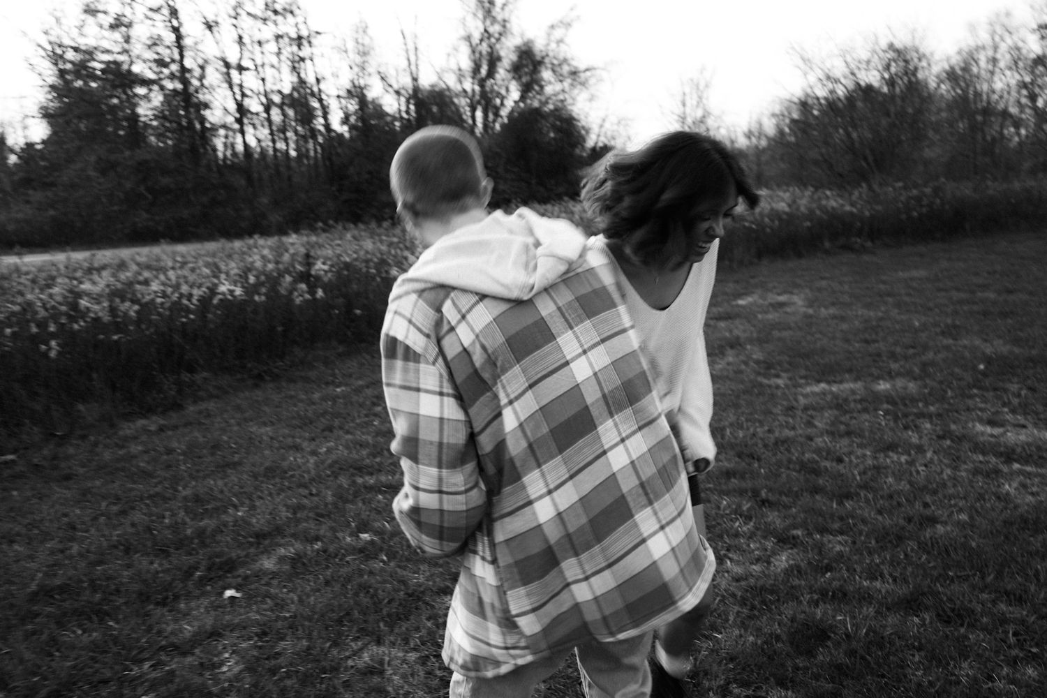Black and white photo of a couple in a field walking away, wearing casual clothing.