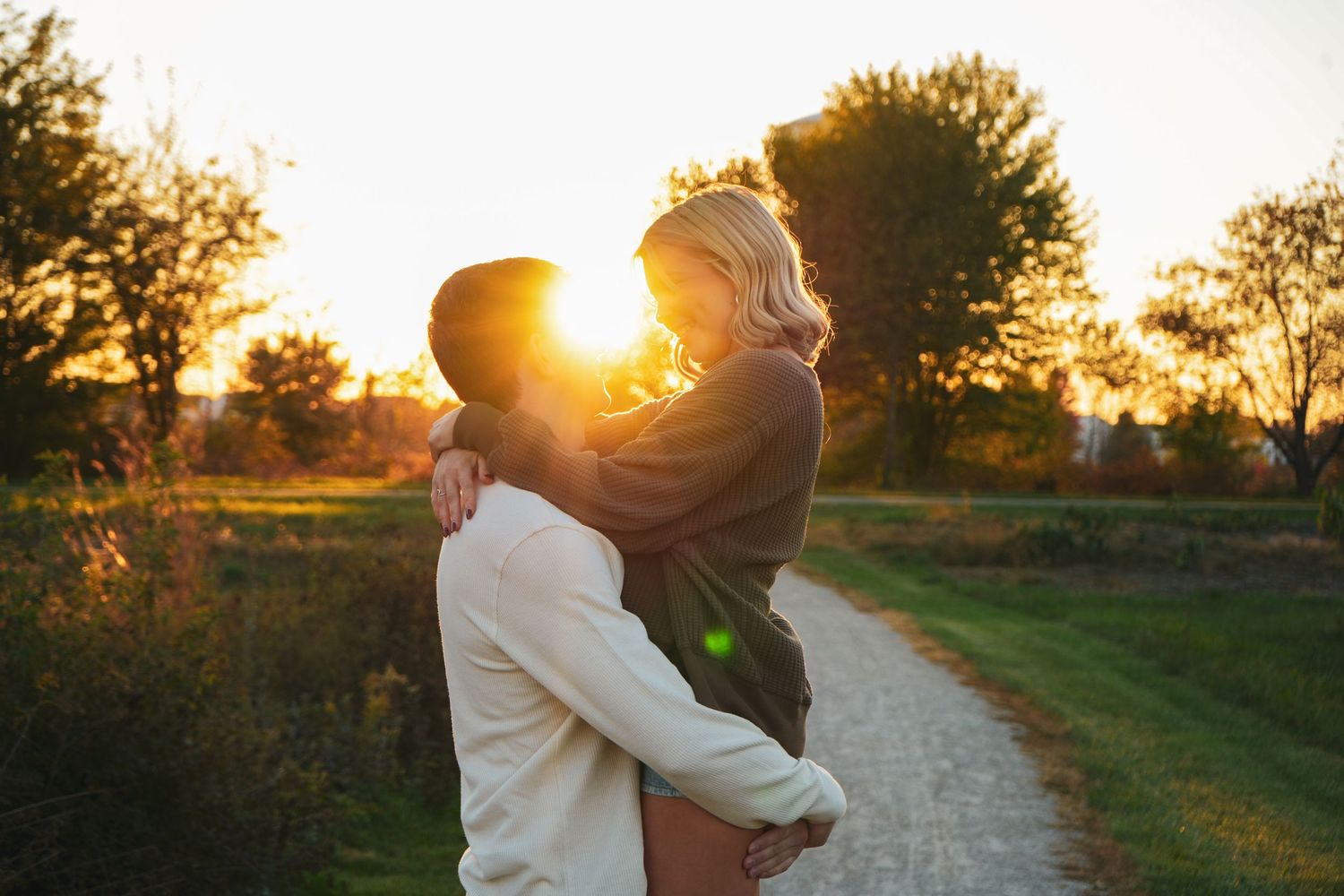 A romantic sunset photoshoot showing silhouettes embracing in a rustic outdoor setting with golden light.