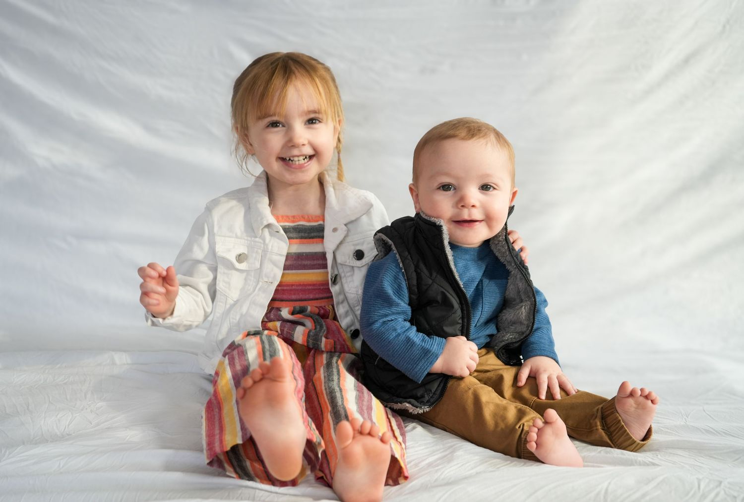 Two young children sitting together against white background wearing casual clothing.