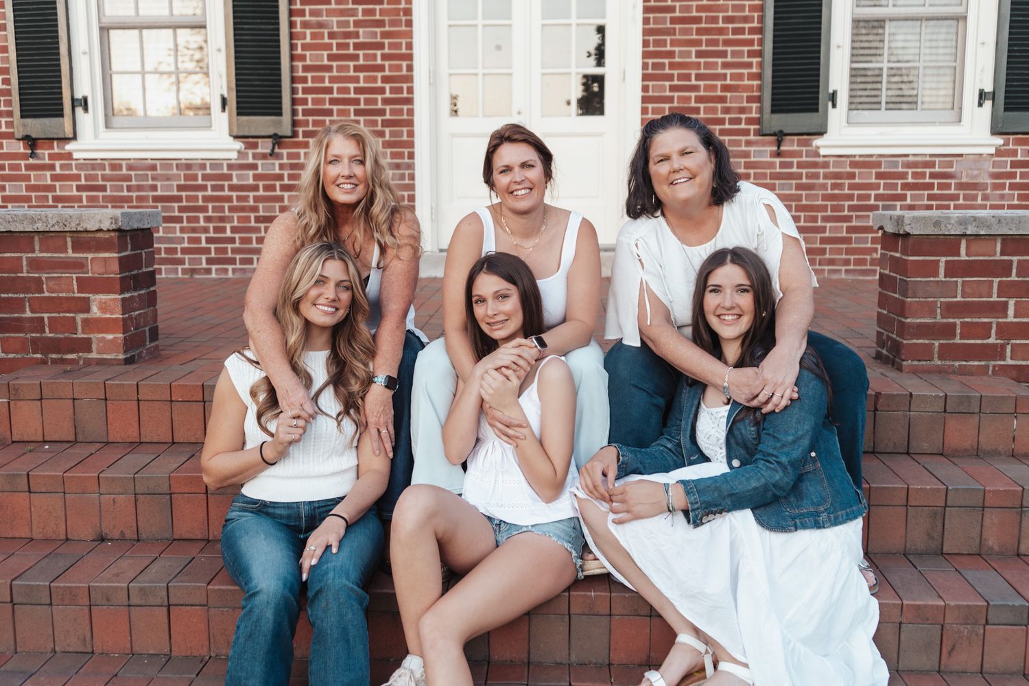 Group sitting on brick steps wearing coordinated white and denim outfits.