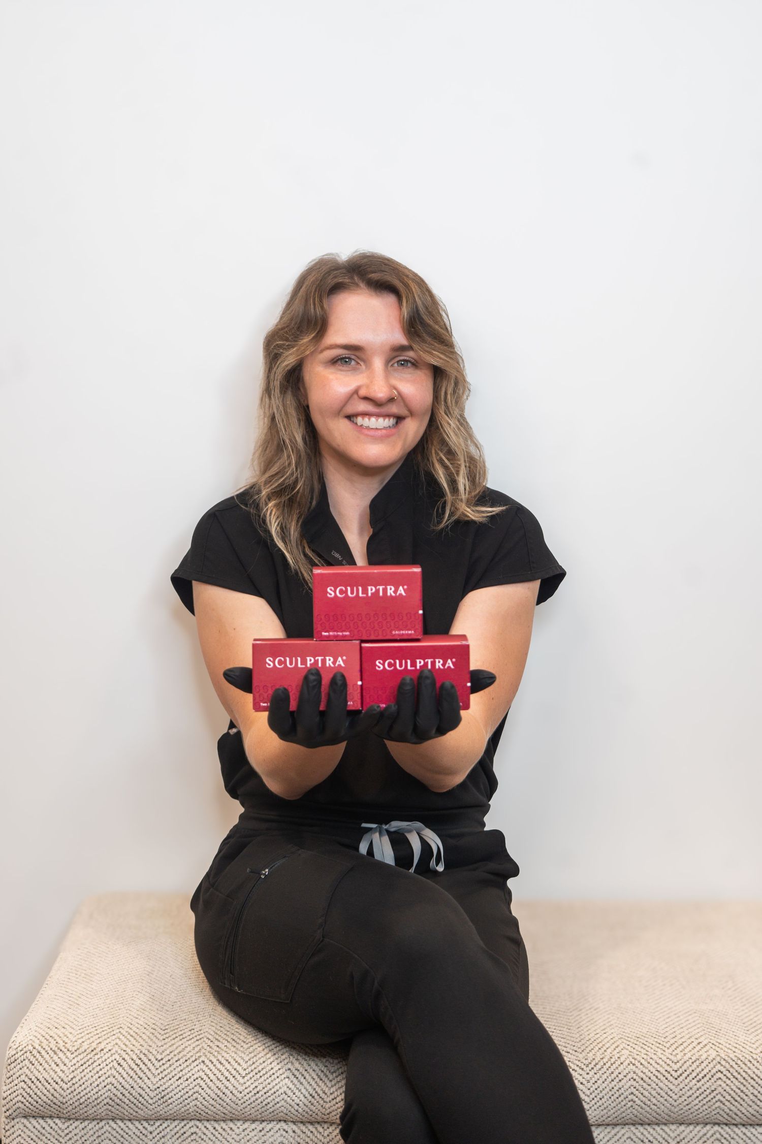 Someone wearing black sits on a beige couch holding red Sculpflex product books in different relaxed poses.