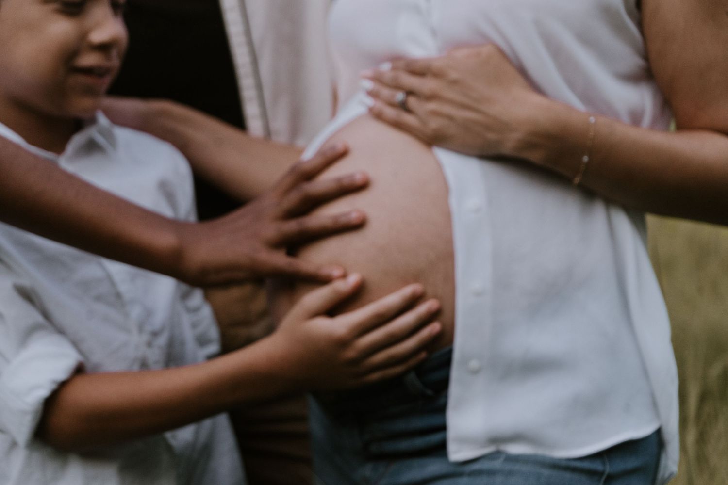 Multiple hands lovingly touch a pregnant belly in an intimate family maternity photograph.