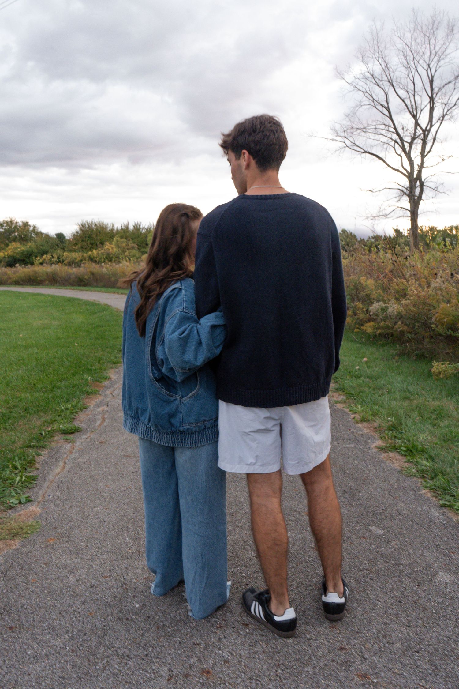 A couple in casual wear walking together on a gravel path through a scenic countryside landscape.