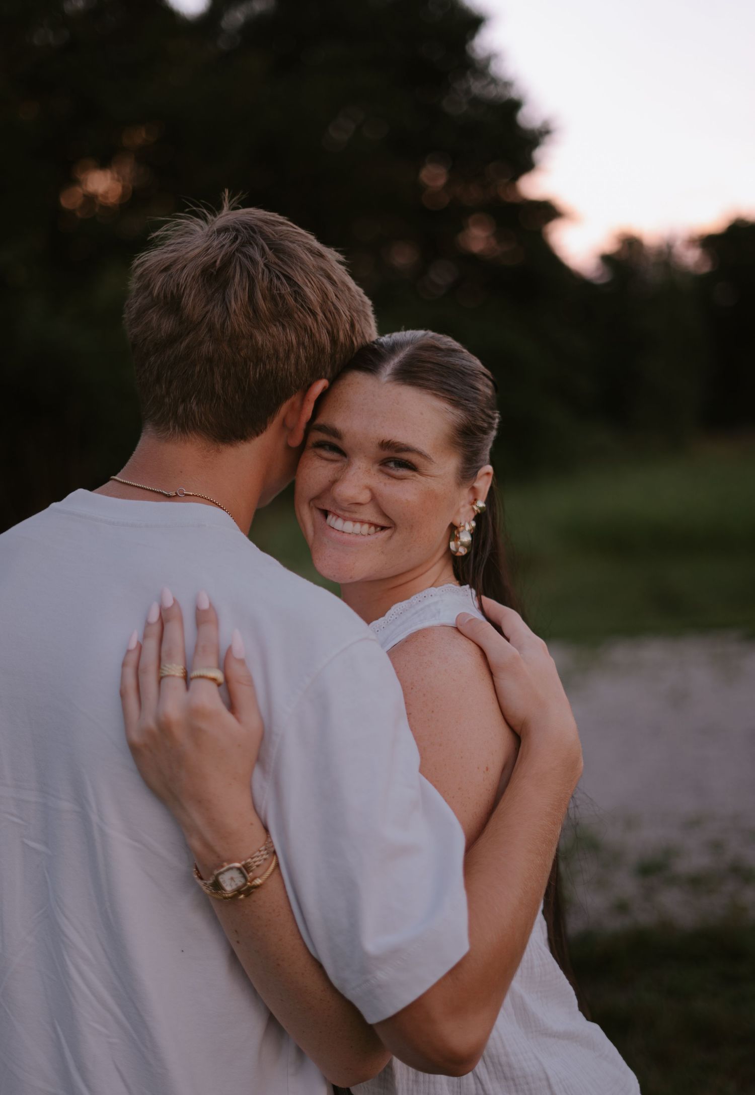 Couple embracing at sunset, woman smiling over mans shoulder outdoors.