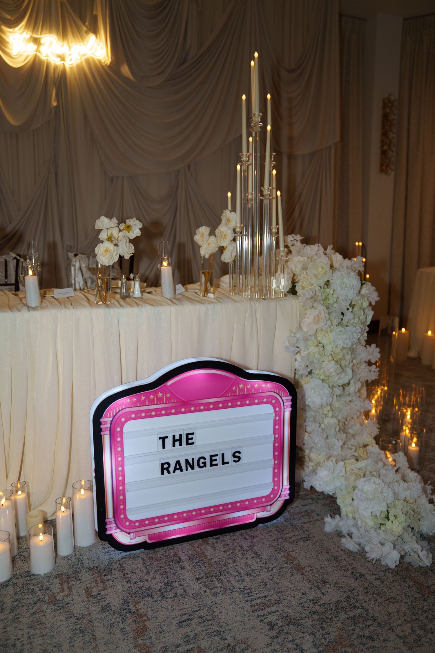 The Rangels wedding reception sweetheart table decorated with white flowers, candles, and a pink marquee sign.