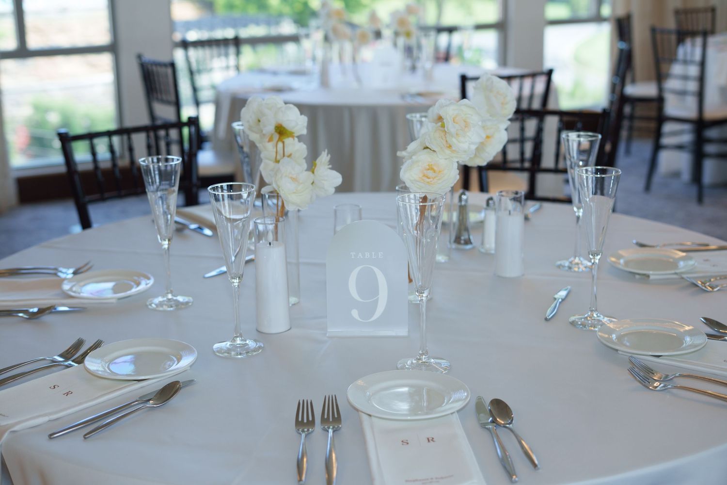 Elegant wedding reception table setting with white linens, floral centerpieces, and a number 9 table card.