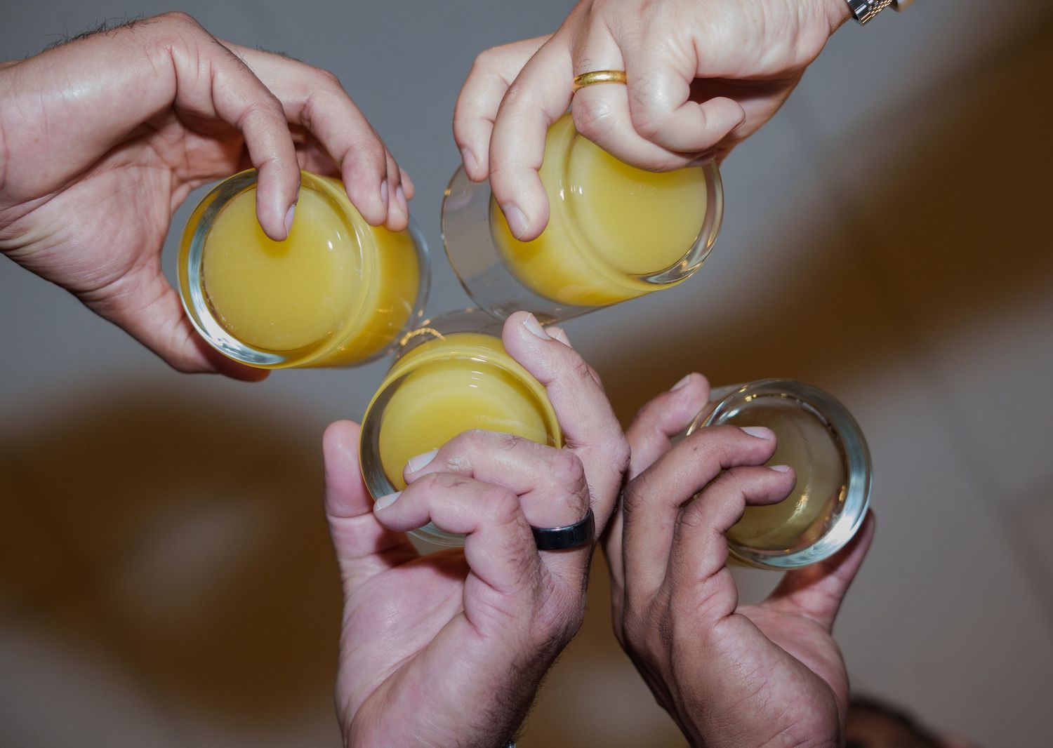 Four hands holding glasses of fresh orange juice together in a celebratory toast from above.
