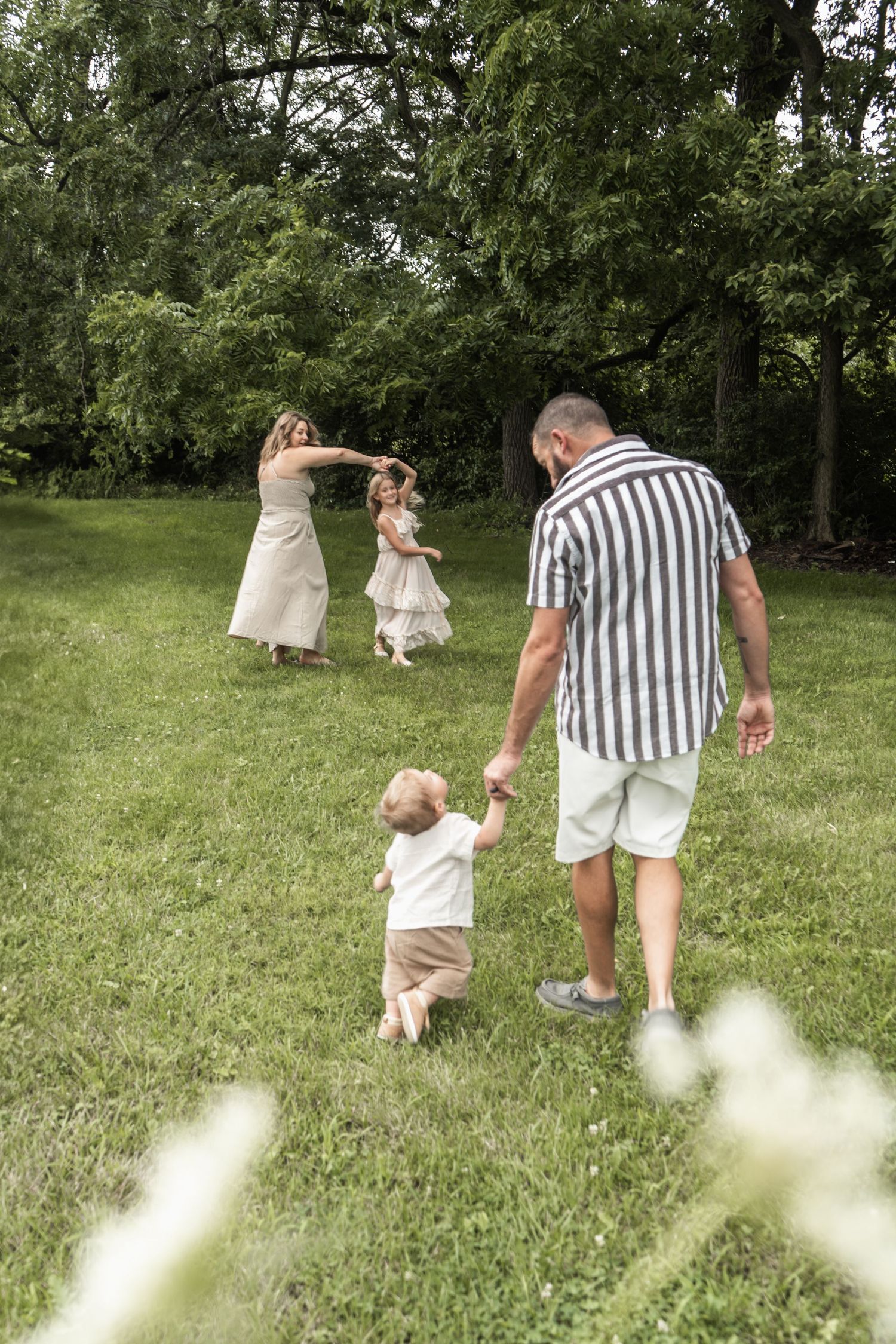A family dances together on a summer day in a lush green backyard surrounded by trees.