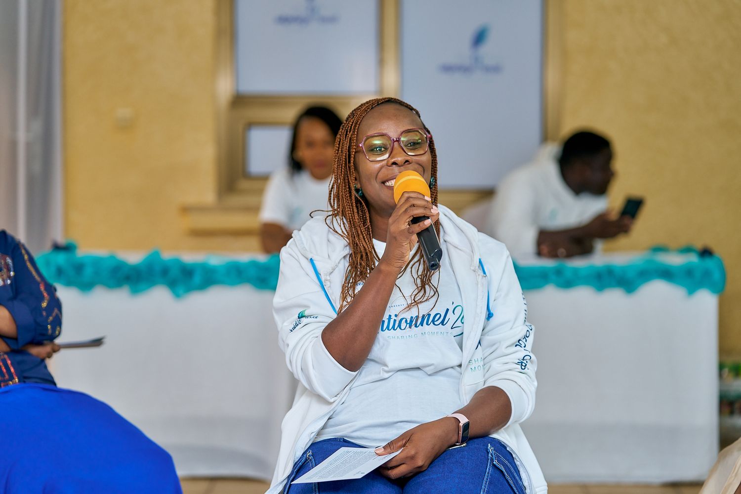 Person in glasses holding orange microphone during indoor presentation, a sharing moment called intentionnel