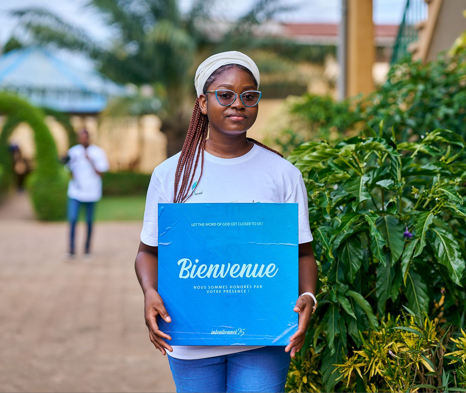 People holding blue welcome signs on outdoor walkway with greenery at sharing moment called intentionnel