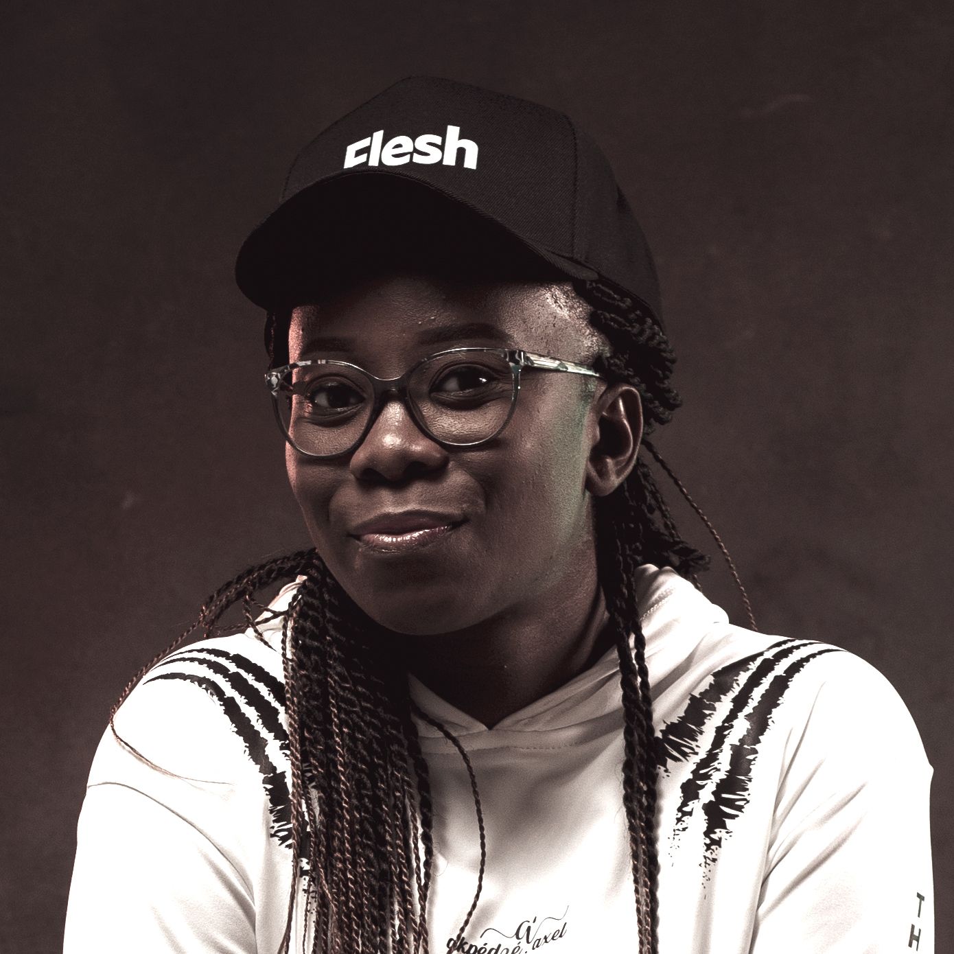 Portrait of person wearing glasses and black baseball cap with 'desh' text against dark background.