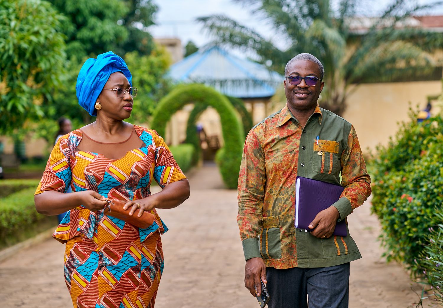 Group in colorful African prints gathered outdoors near palm trees at sharing moment called intentionnel