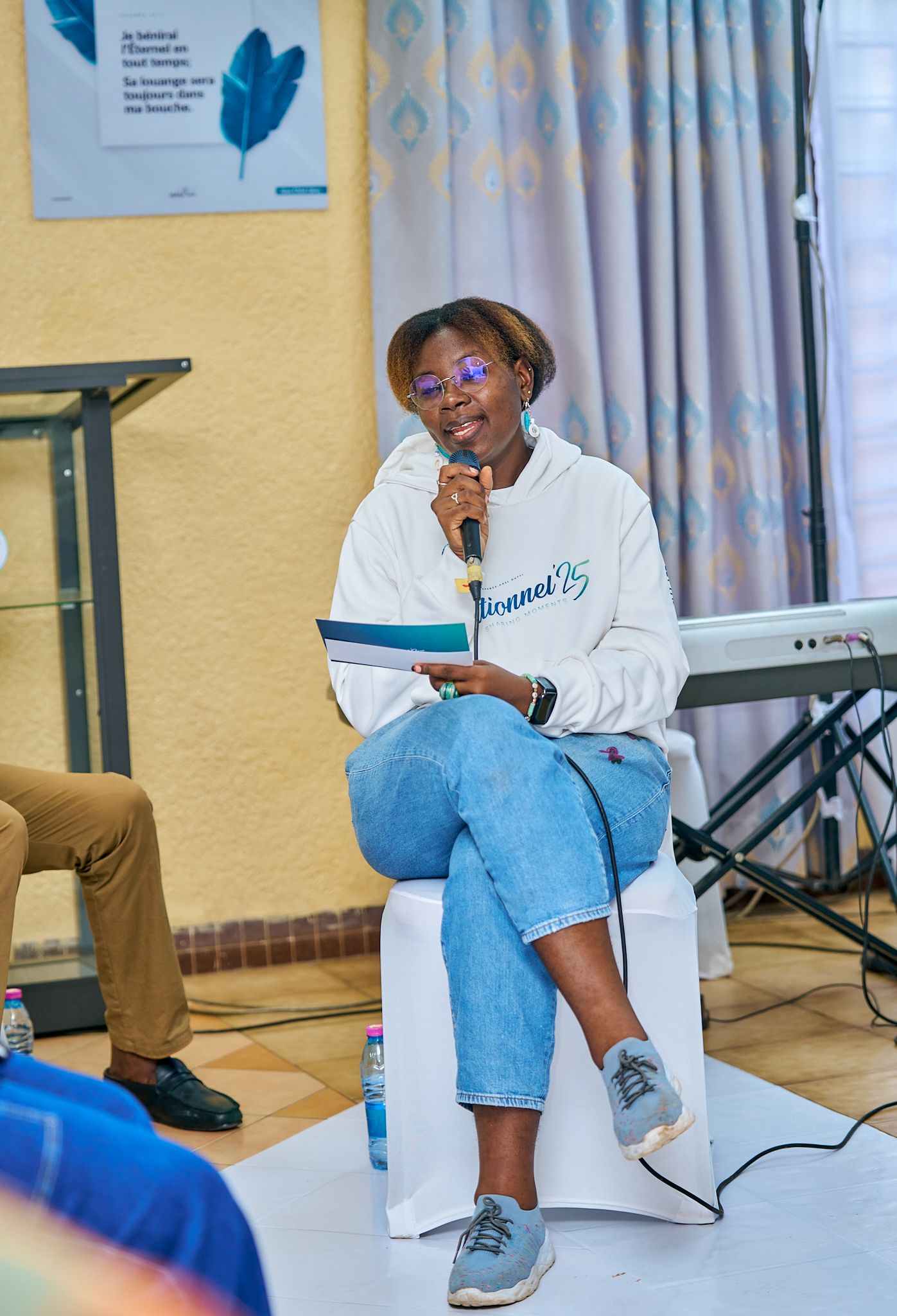 Speaker in white sweatshirt and jeans holding microphone during presentation at sharing moment called intentionnel