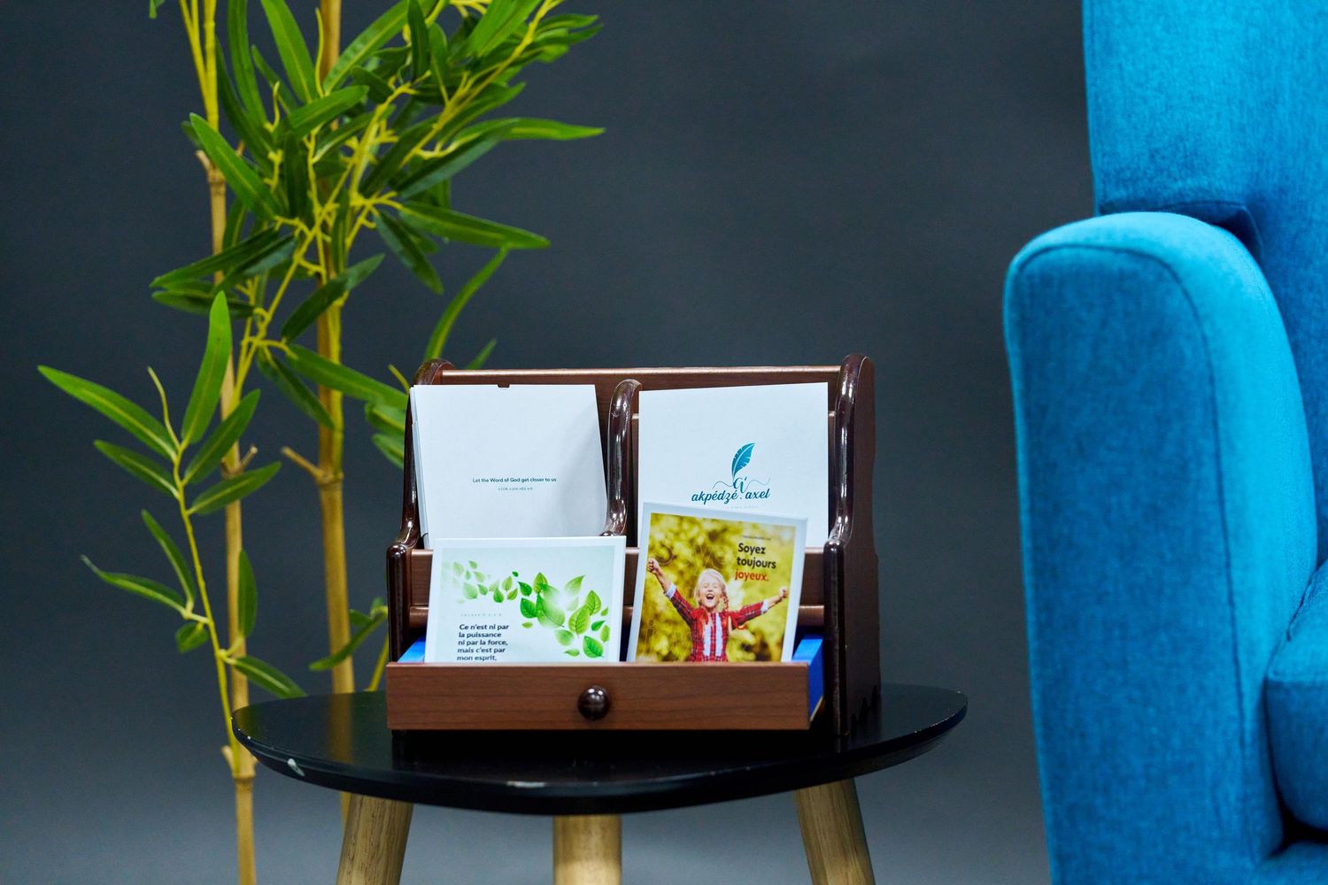 Marketing materials displayed on black side table with blue armchair and bamboo plant. Verset biblique illustré, illustrated biblical verse,