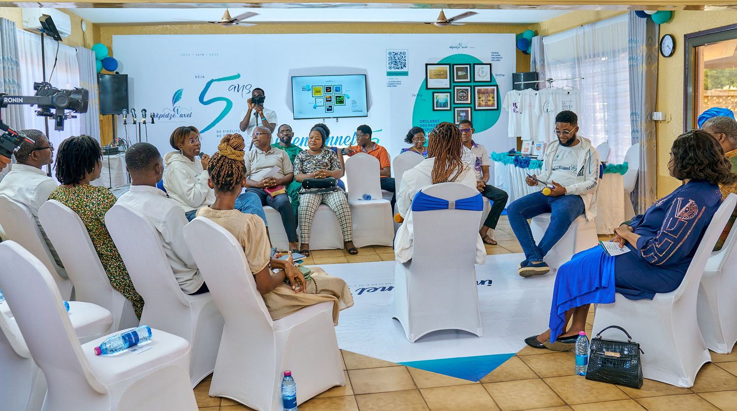 People seated in white chairs attend a sharing moment called intentionnel in a blue-walled room with educational posters and decorations